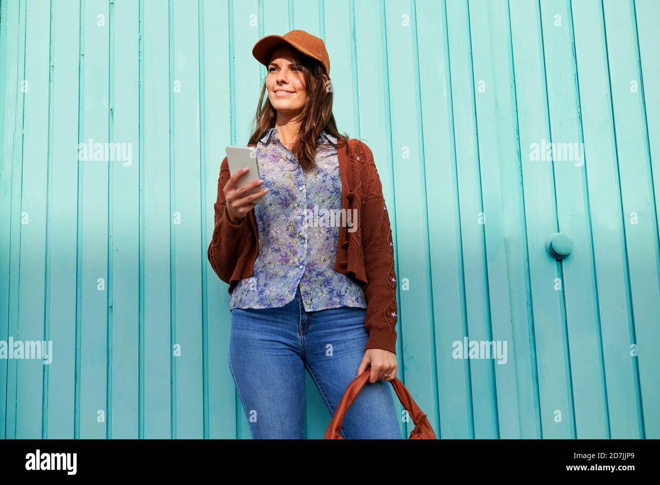 Junge Frau mit Handy, während sie gegen blaues Metall stehen Tür Stockfoto
