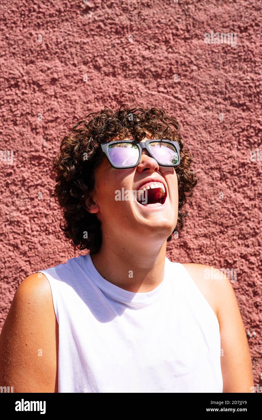 Teenager trägt Sonnenbrille mit offenem Mund gegen braune Wand Stockfoto