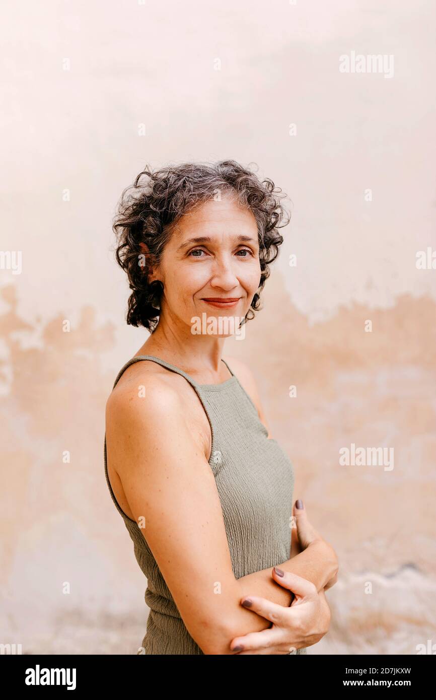 Reife Frau mit gekreuzten Armen, die gegen die Wand stehen Stockfoto