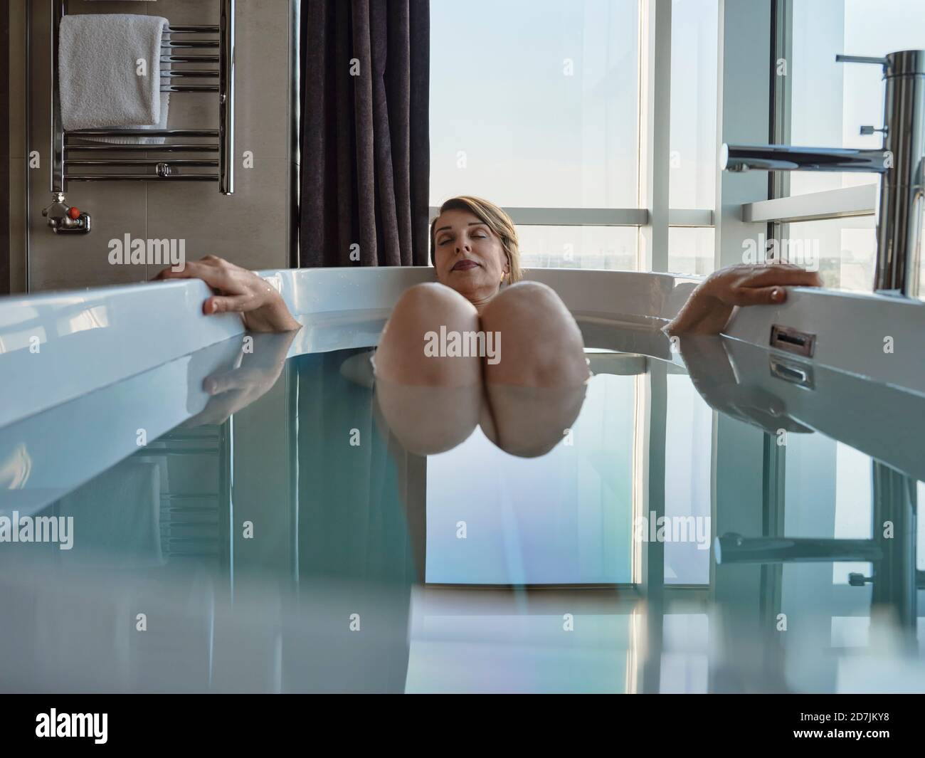 Rentnerin, die in der Badewanne gegen das Fenster im Luxus baden Hotelzimmer Stockfoto