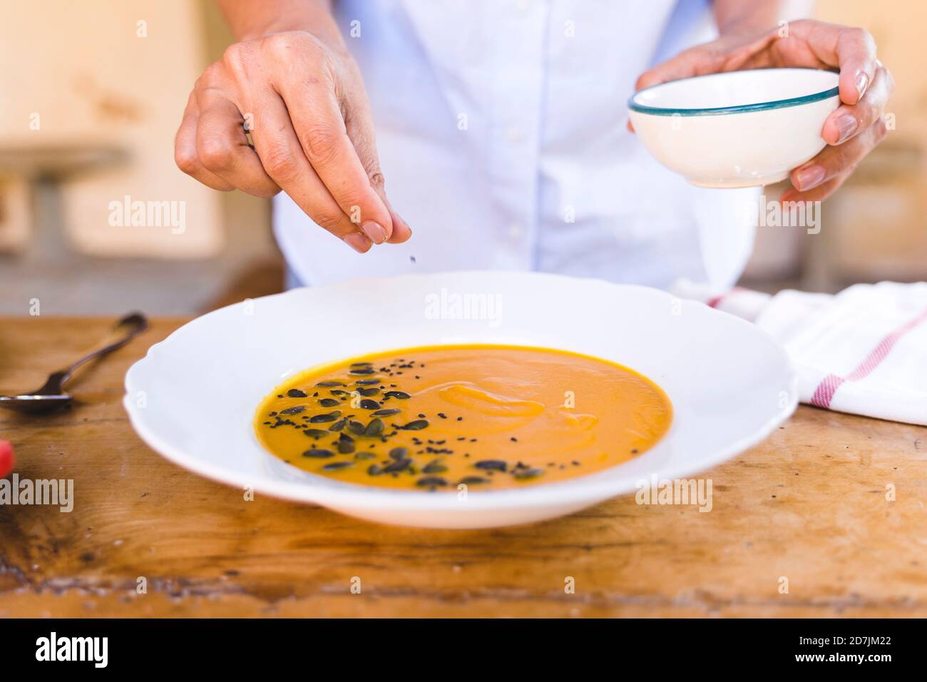 Frau, die Sesamsamen in die Suppe legt, während sie am Tisch steht Stockfoto