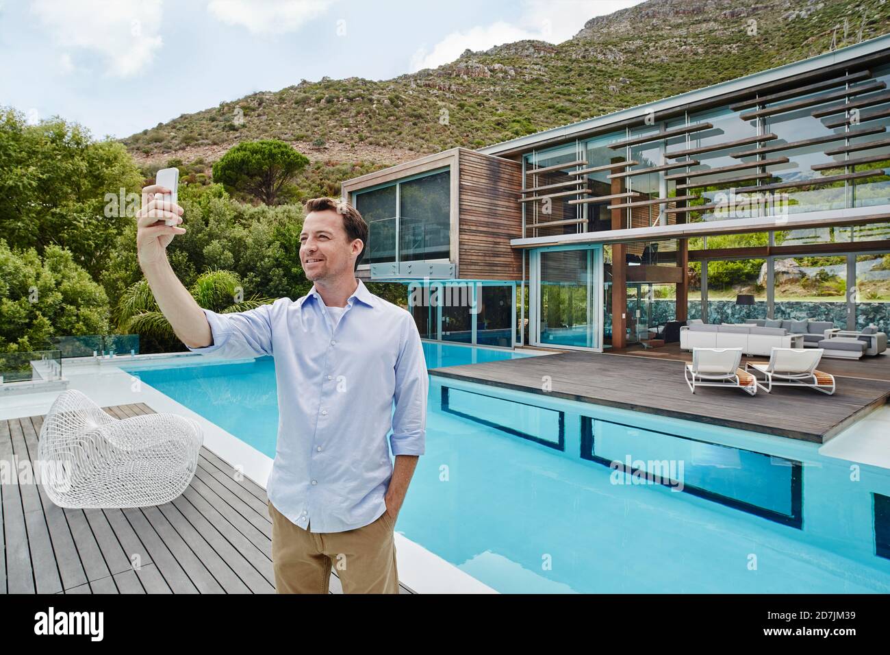 Reifer Mann, der Selfie auf dem Smartphone nimmt, während er dagegen steht Modernes Haus Stockfoto