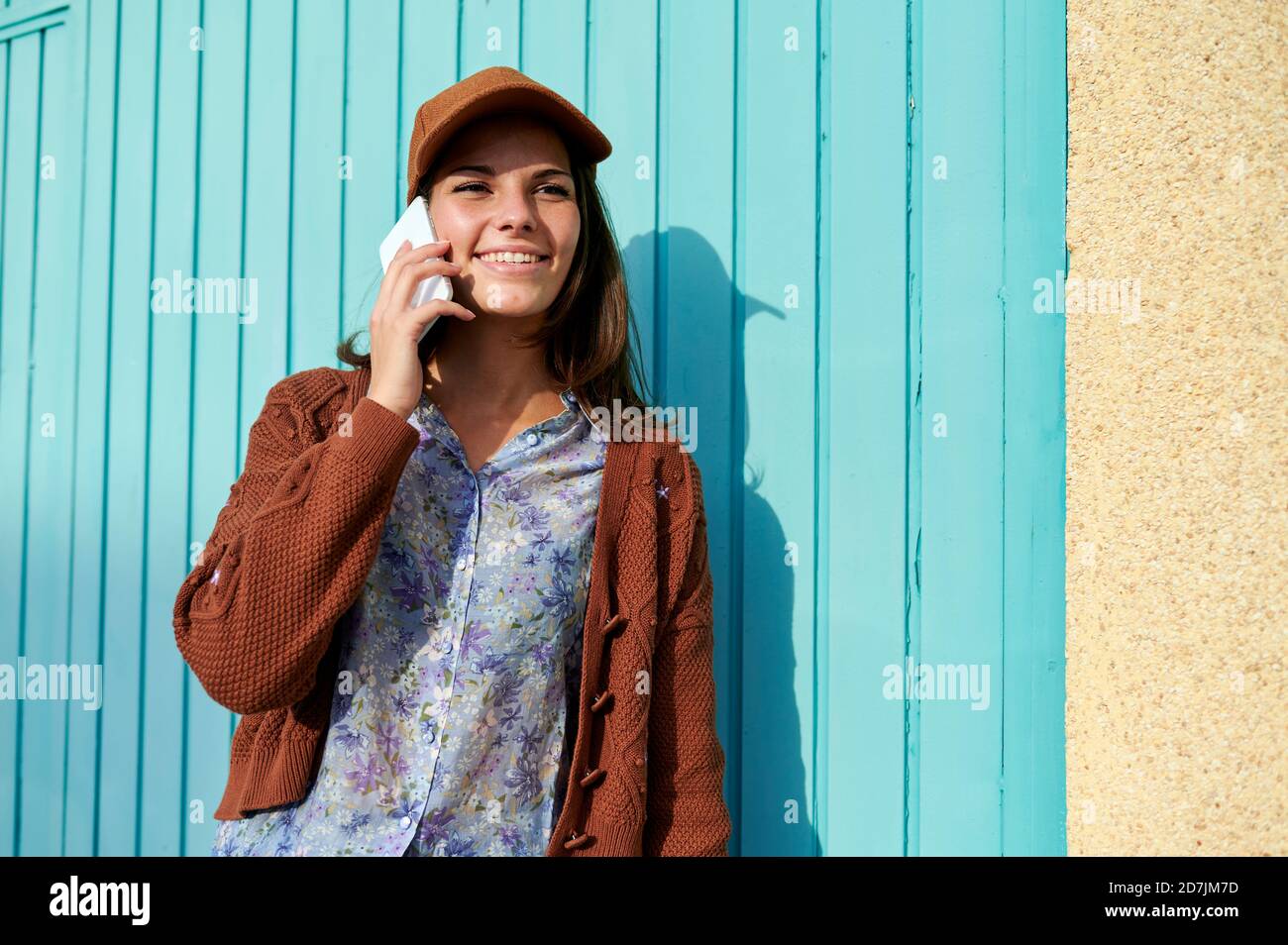 Junge Frau lächelt, während sie am Telefon gegen blaues Metall spricht Tür Stockfoto