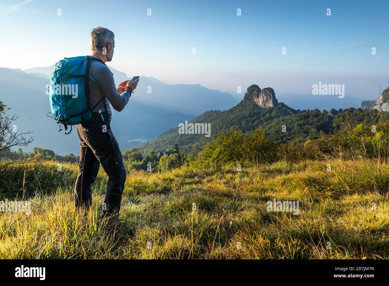 Reifer Mann mit Smartphone beim Wandern auf dem Berg bei Sonnenaufgang, Orobie, Lecco, Italien Stockfoto