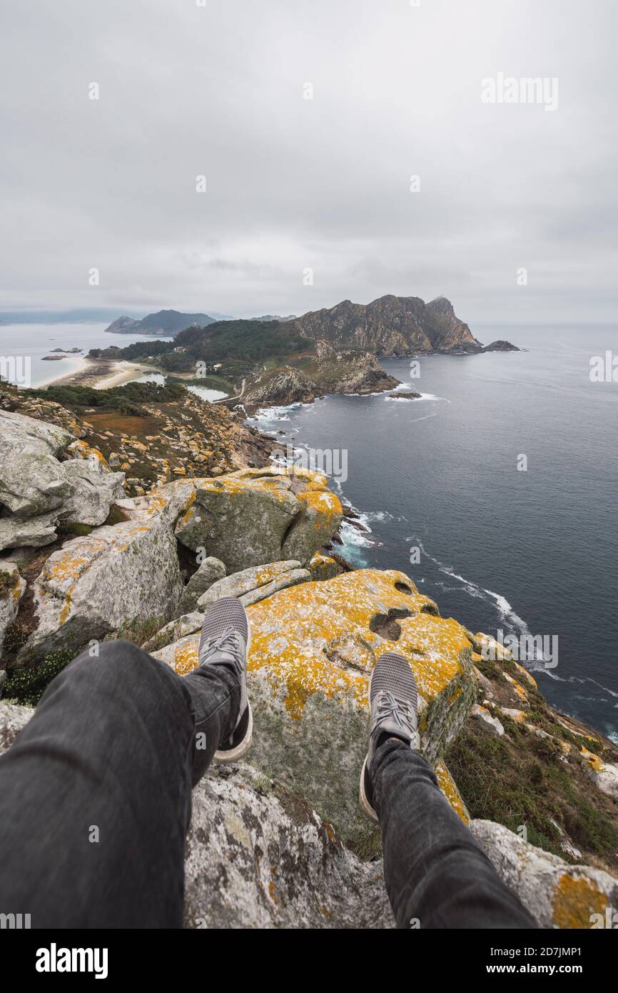 Niedriger Abschnitt des jungen männlichen Touristen über Felsformation gegen bewölkten Himmel, Cíes Inseln, Vigo, Pontevedra Provinz, Galicien, Spanien Stockfoto