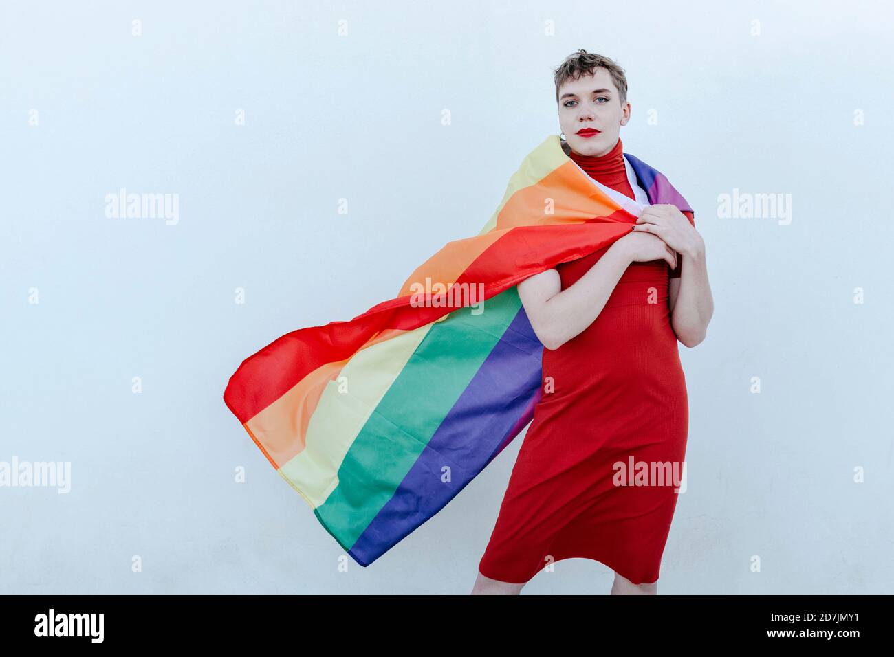 Nicht-binäre Person trägt Regenbogenfahne um den Hals, während sie gegen Weißer Hintergrund Stockfoto