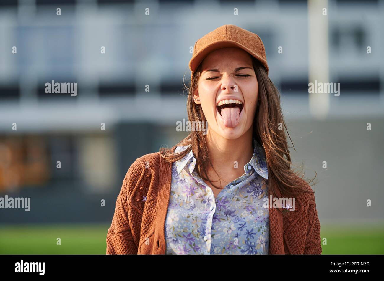 Junge Frau, die in der Stadt steht und die Zunge herausstreckt Stockfoto