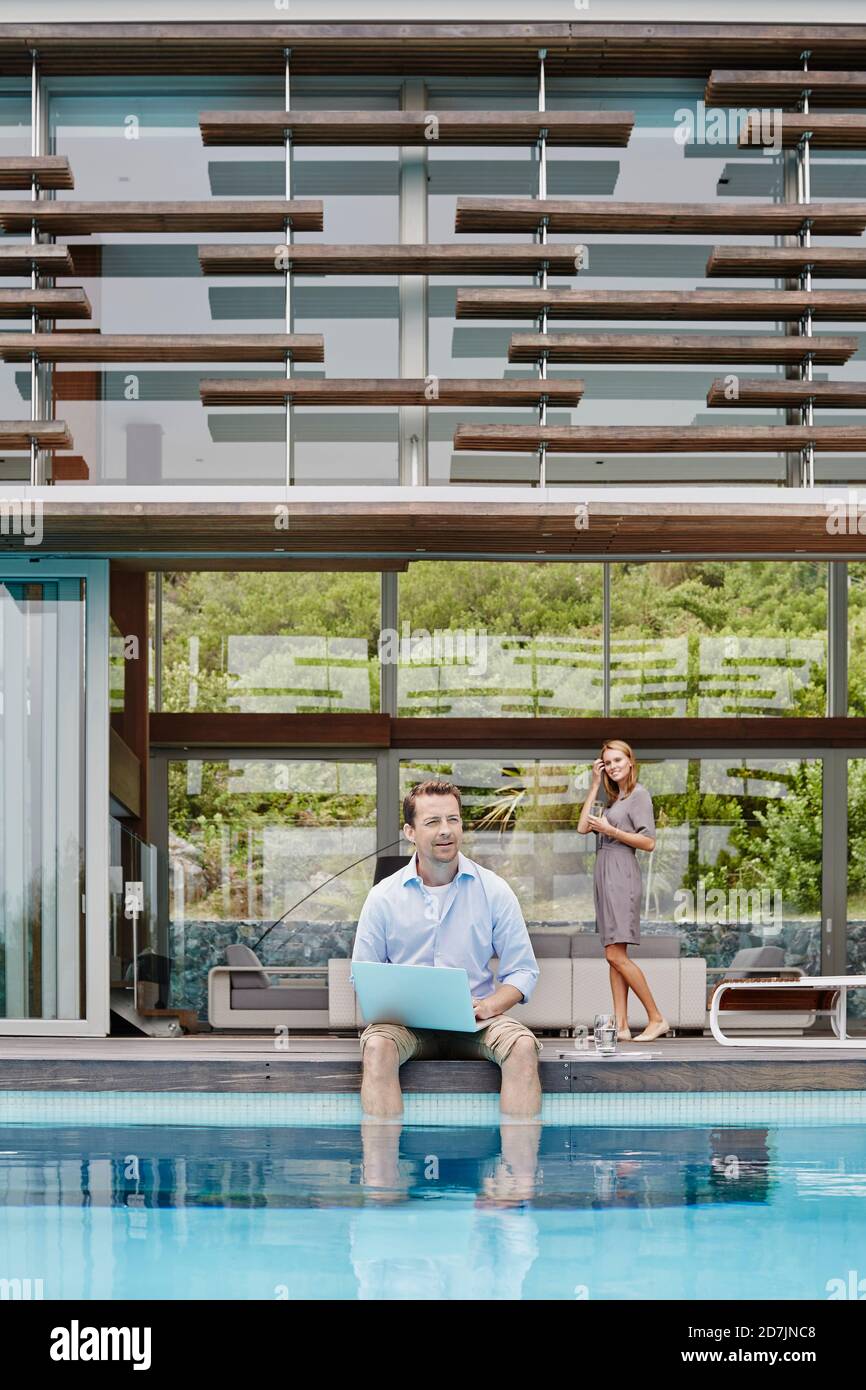 Der Mann, der am Laptop arbeitet, schaut weg, während er gegen die Moderne sitzt Haus Stockfoto