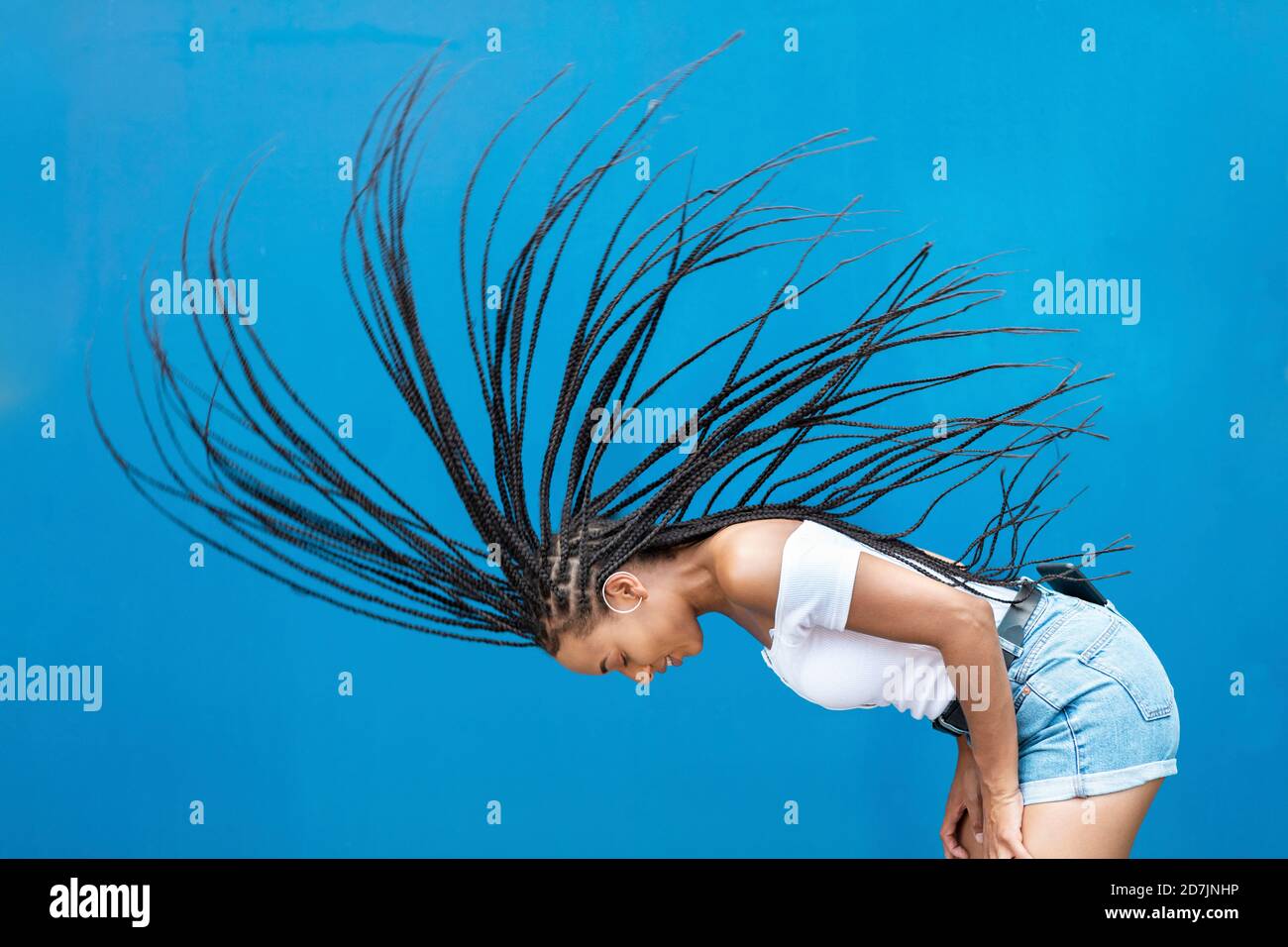 Frau wirft Haare gegen die blaue Wand Stockfoto