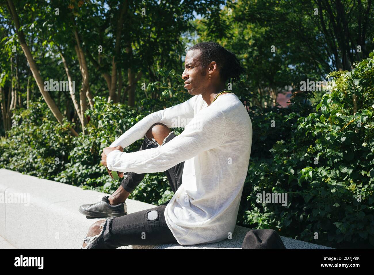 Mann, der auf einer Stützmauer im Park sitzt Stockfoto