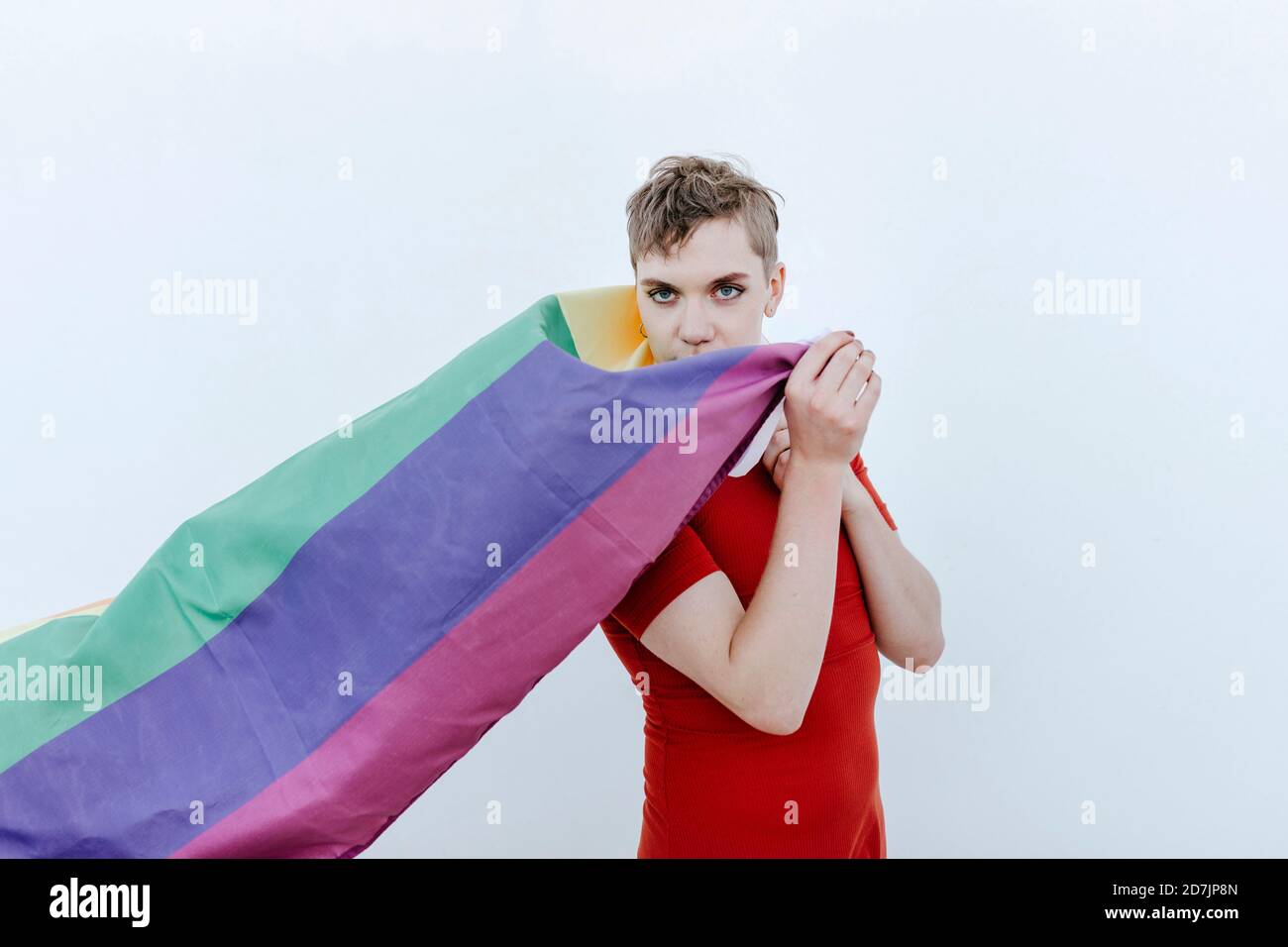 Nicht-binäre Person hält Regenbogenfahne, während sie vor weißem Hintergrund steht Stockfoto