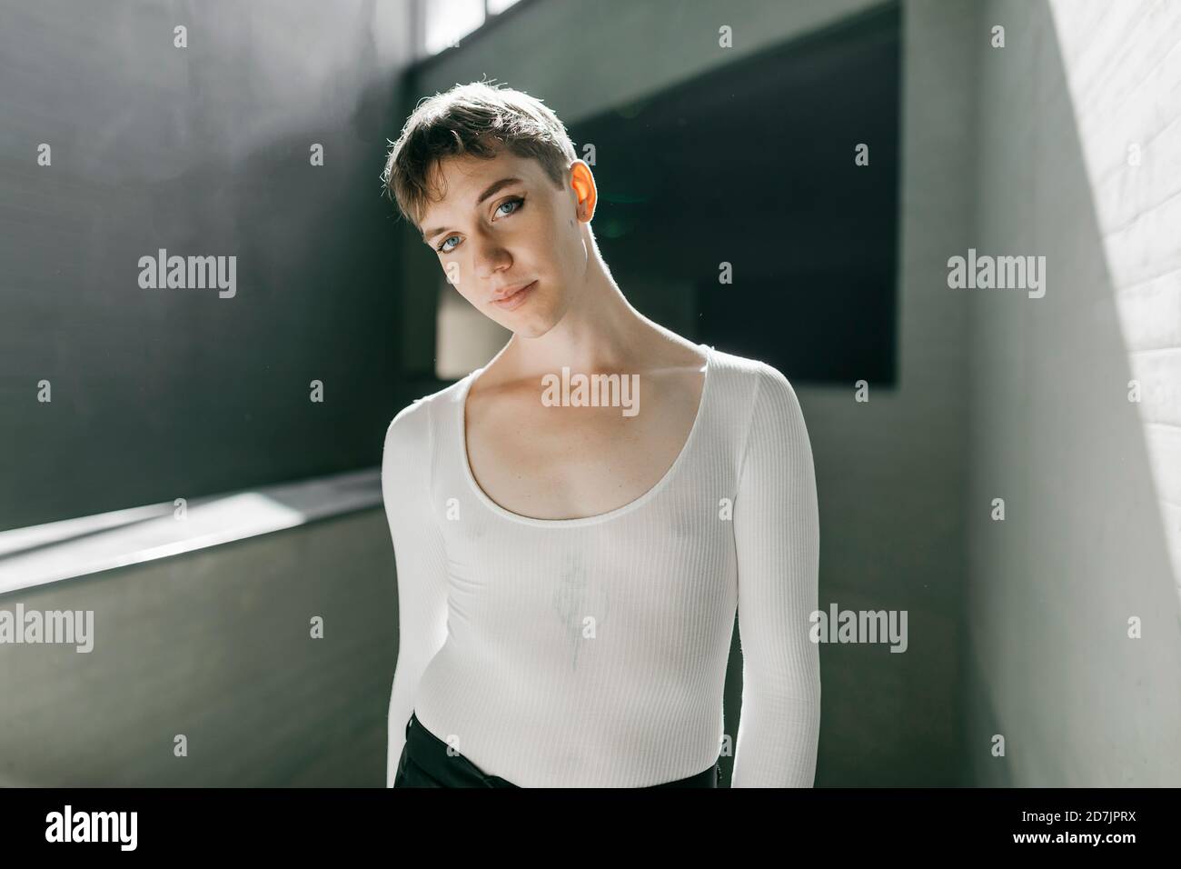 Trans junger Mann in weißem Trikot im Keller stehend Stockfoto