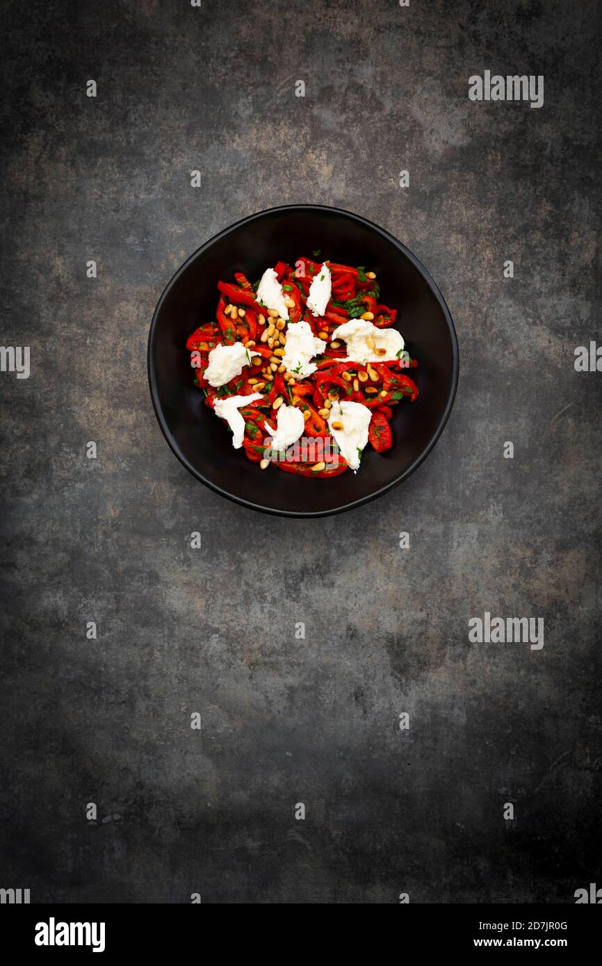 Schüssel vegetarischer Salat mit roten Paprika, Mozzarella, gerösteten Pinienkernen, Petersilie und Schnittlauch Stockfoto