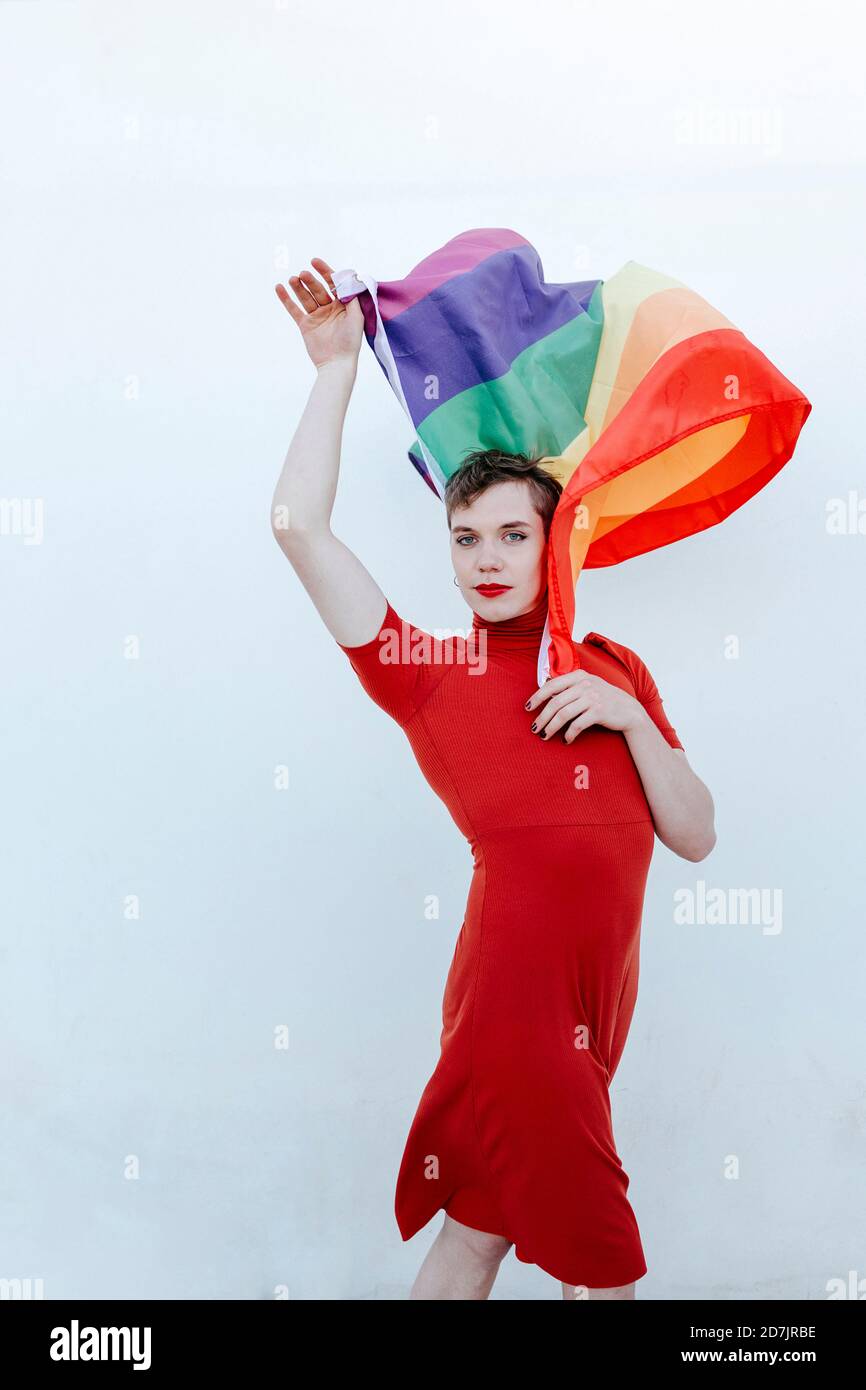Nicht-binäre Person winkt Regenbogenfahne, während vor weißem Hintergrund stehen Stockfoto