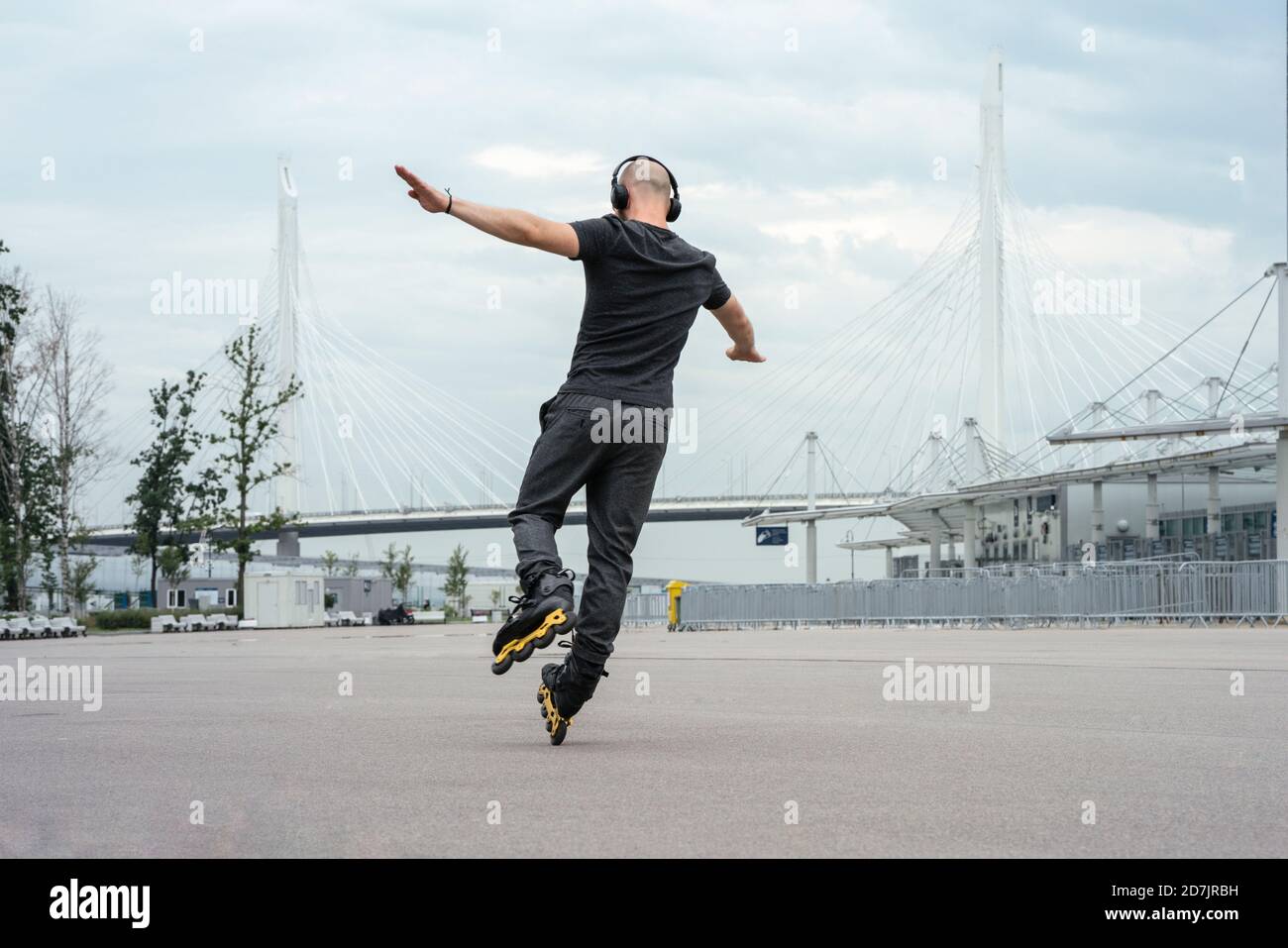 Junger Mann mit ausgestreckten Armen hört Musik beim Inline-Skaten Auf der Straße Stockfoto