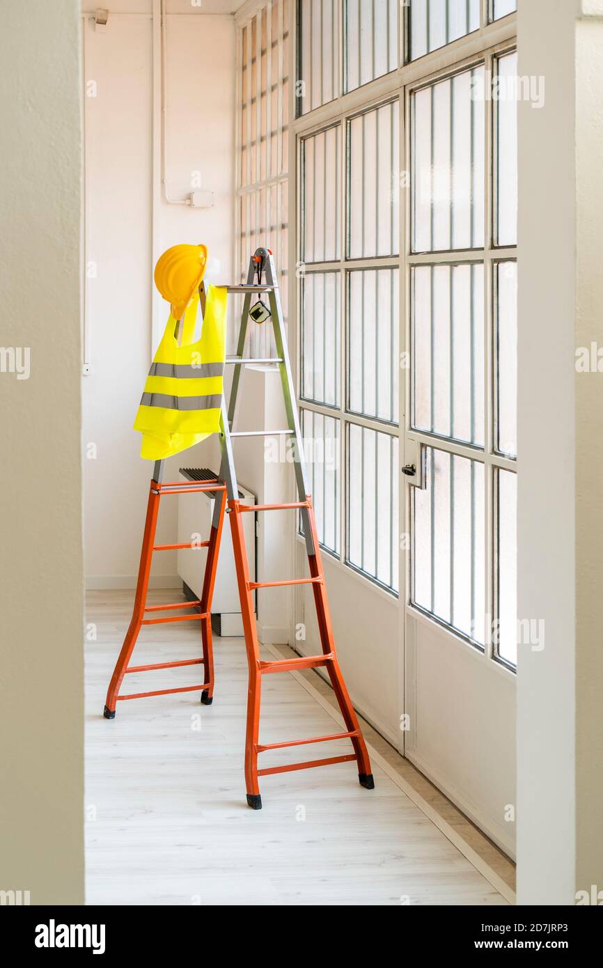 Hardhut und reflektierende Weste hängen an der Leiter im leeren Studio Stockfoto