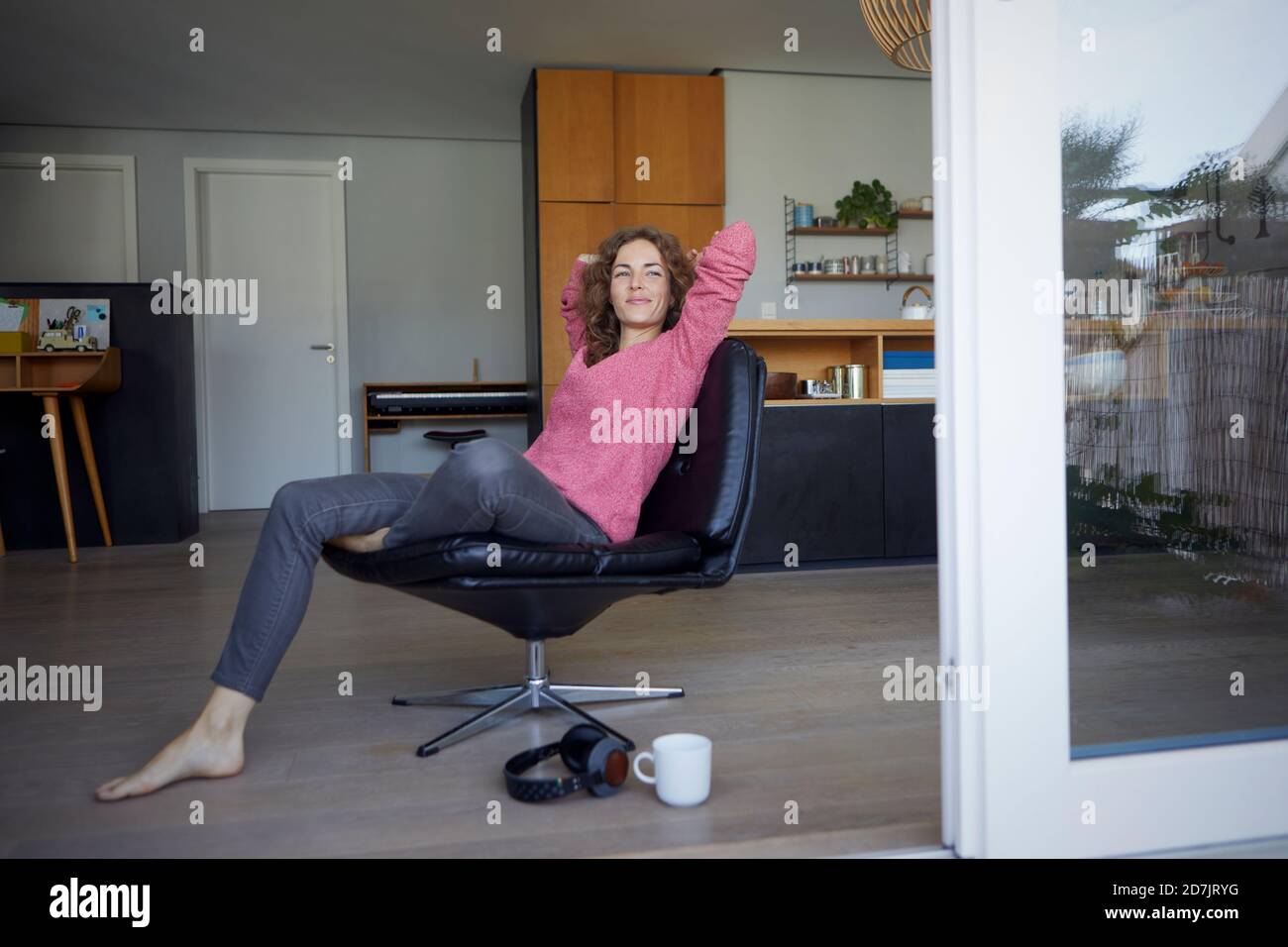 Lächelnde Frau mit den Händen hinter dem Kopf auf dem Stuhl ruhen Zu Hause Stockfoto