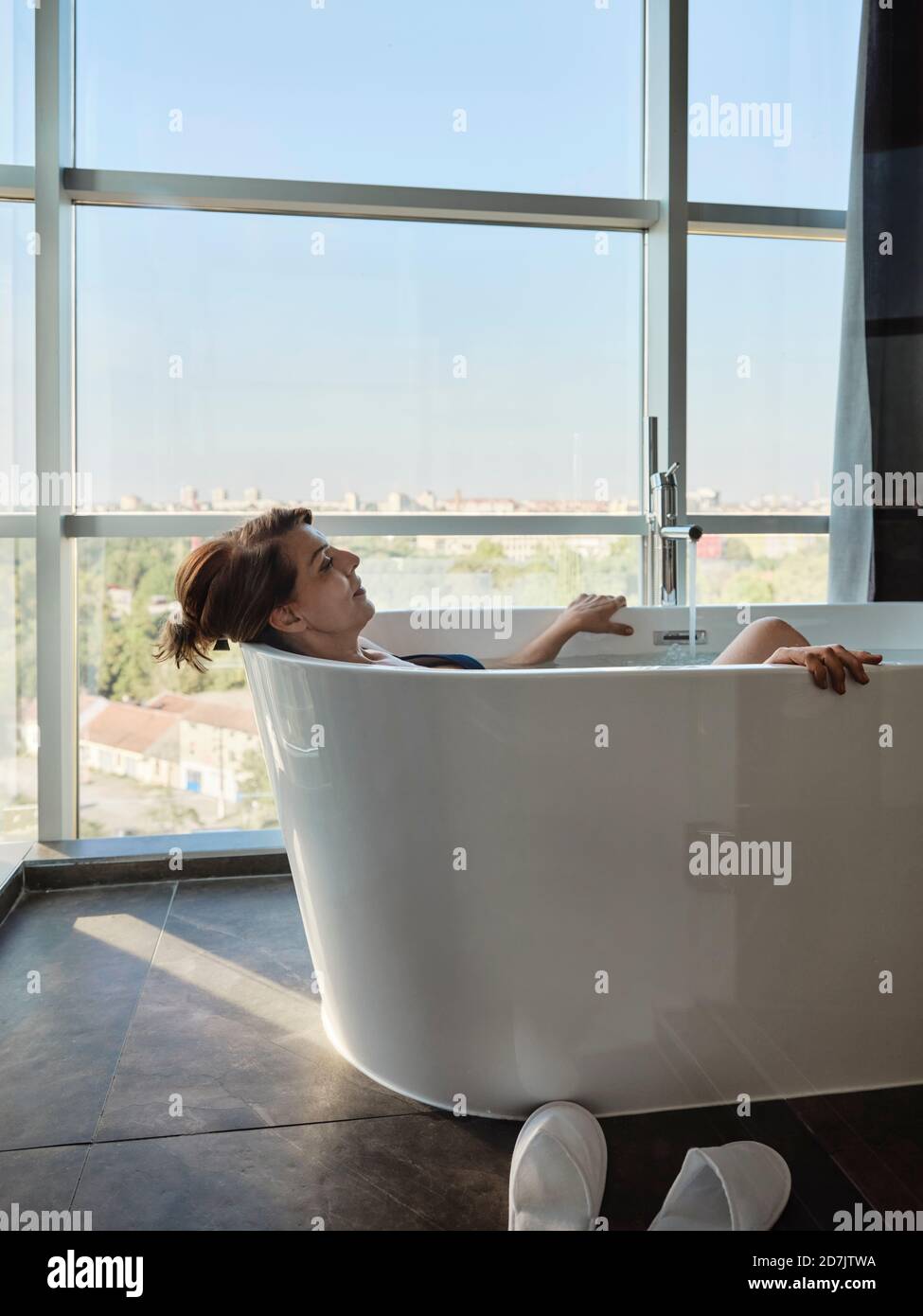 Entspannte ältere Frau im Ruhestand, die im Urlaub in der Badewanne baden ging Am Fenster des Luxushotels Stockfoto