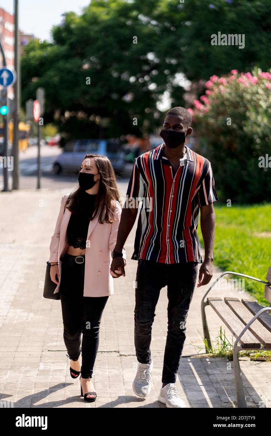 Junges Paar in Gesichtsmasken, die Hände beim Gehen halten Stadt während der COVID-19-Krise Stockfoto