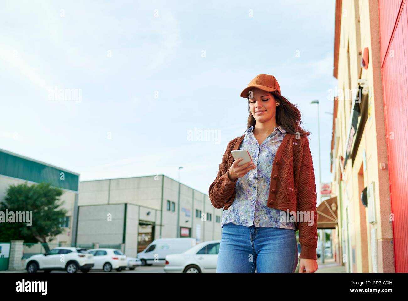Lächelnde Frau mit Mütze mit Handy, während sie im Stehen Stadt Stockfoto
