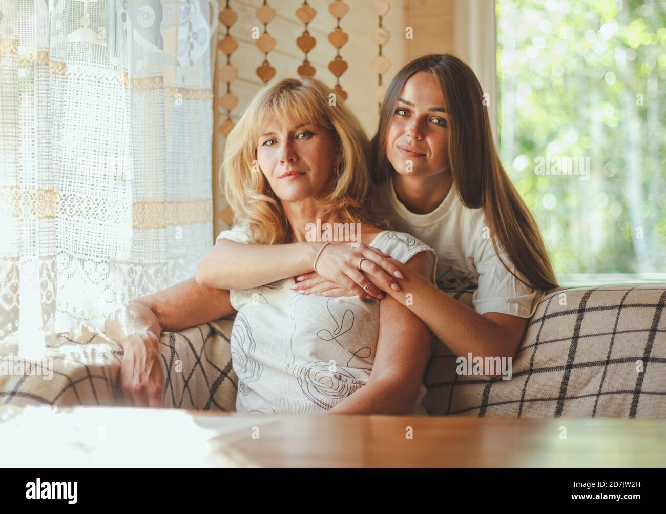 Liebevolle Erwachsene 20s Tochter Umarmung ältere Mutter von hinten während Mutter auf Couch sitzend Menschen posieren Blick auf Kamera lächelnd fühlt sich glücklich, Konzept der mu Stockfoto