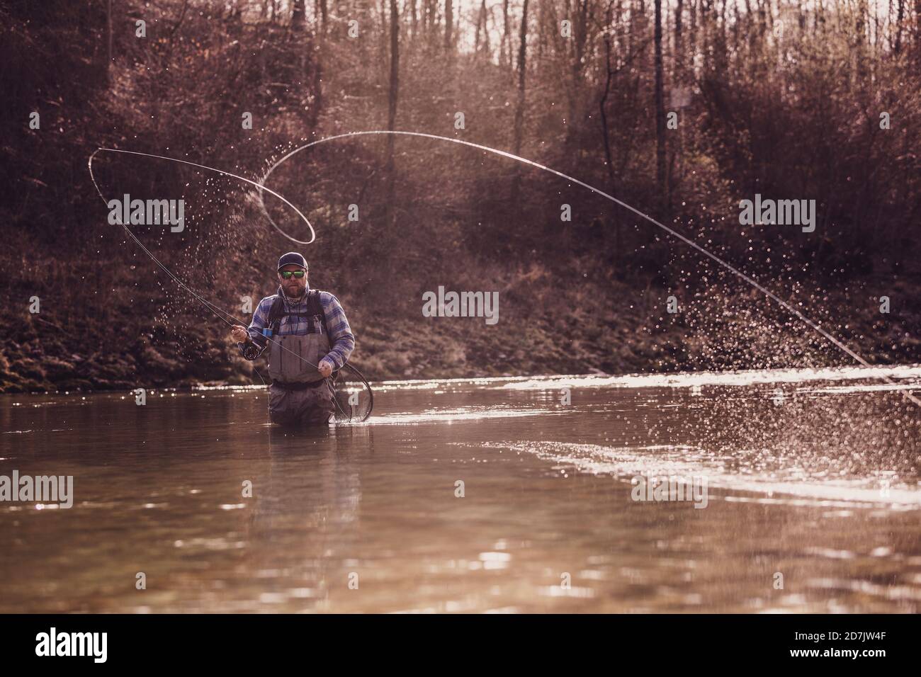 Mid adult man werfen Angelrolle im Fluss zu fangen Fische bei Sonnenuntergang Stockfoto