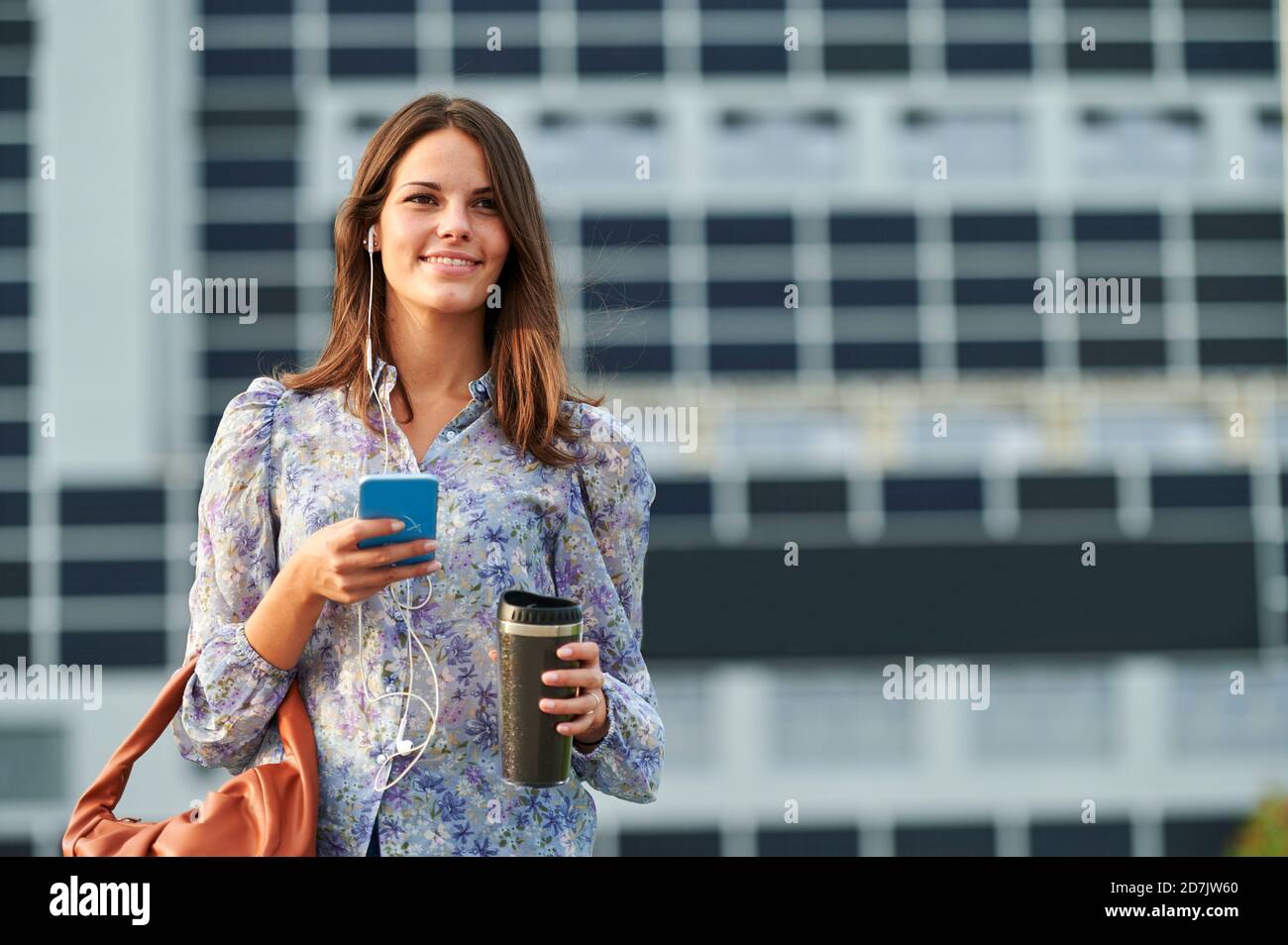 Junge Frau, die Musik hört, während sie das Mobiltelefon in der Stadt benutzt Stockfoto