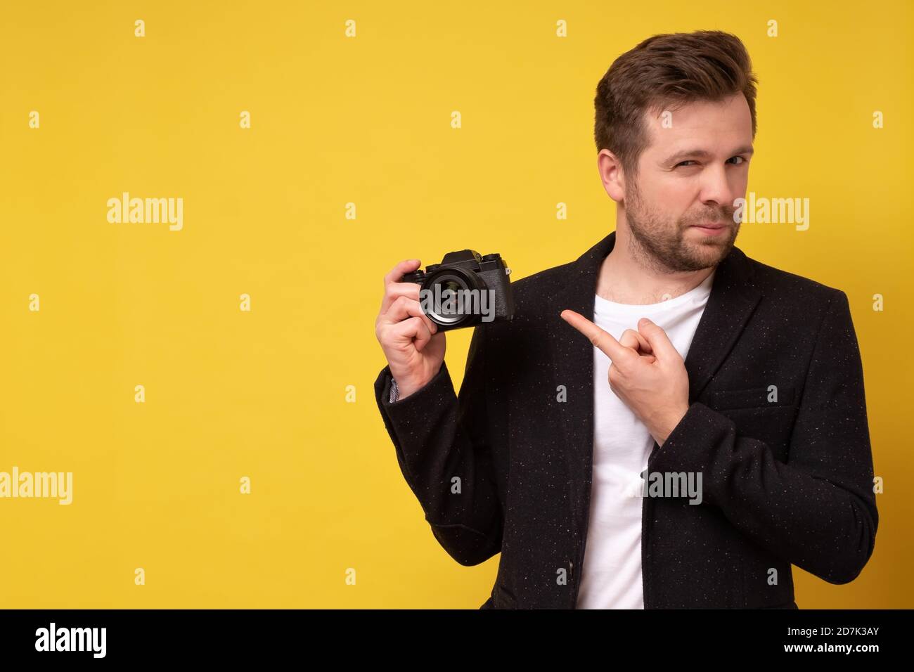 Reisender und Fotograf. Studio Porträt von schönen jungen Mann hält Fotokamera Aufnahme. Gelber schwarzer Boden. Stockfoto