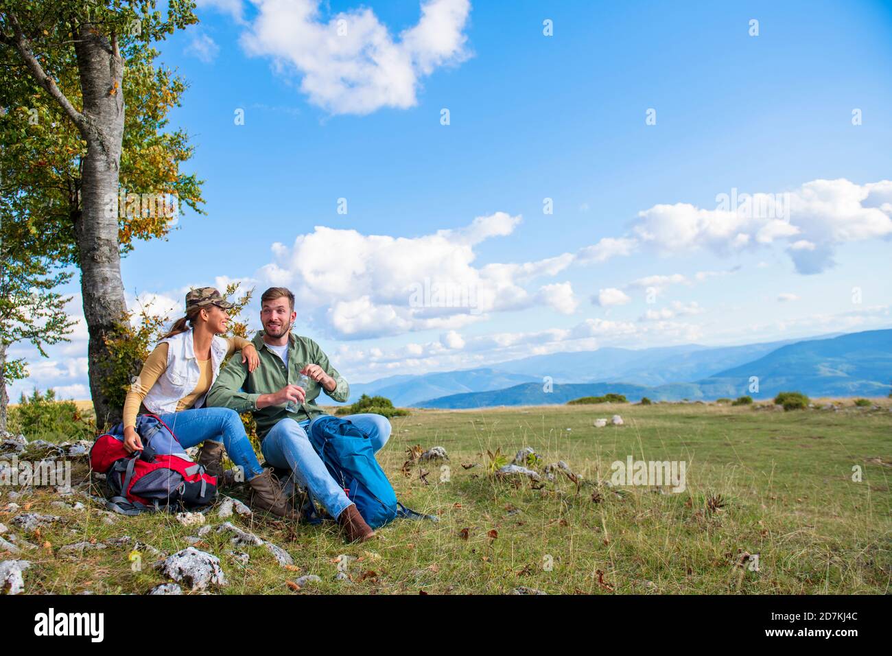Junges Paar Trinkwasser, während er auf den Felsen während der Reisen in die Berge Stockfoto