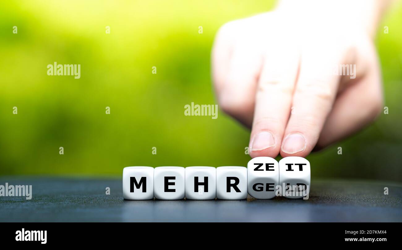 Hand dreht Würfel und ändert den deutschen Ausdruck 'mehr Geld' in 'mehr Zeit'. Stockfoto