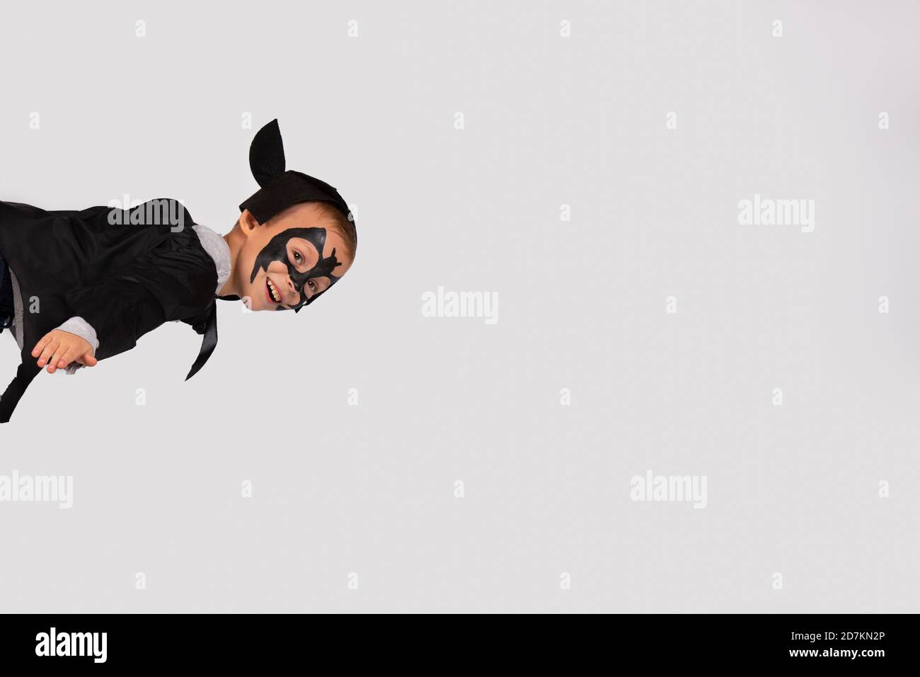 Fröhlicher Junge im schwarzen Fledermaus Kostüm mit Ohren, die wie ein Blitz in den Himmel fliegen. Stockfoto