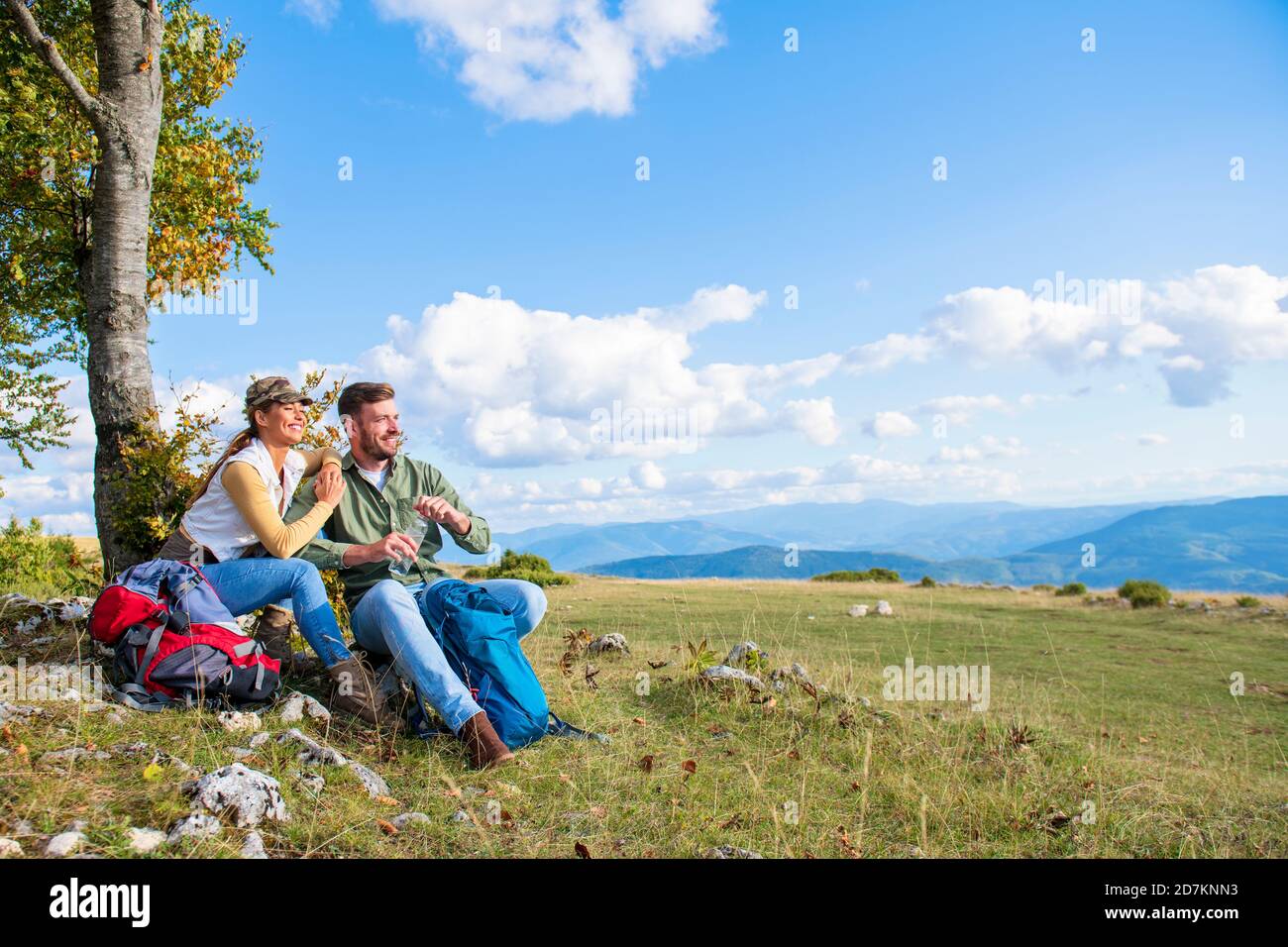 Junges Paar Trinkwasser, während er auf den Felsen während der Reisen in die Berge Stockfoto