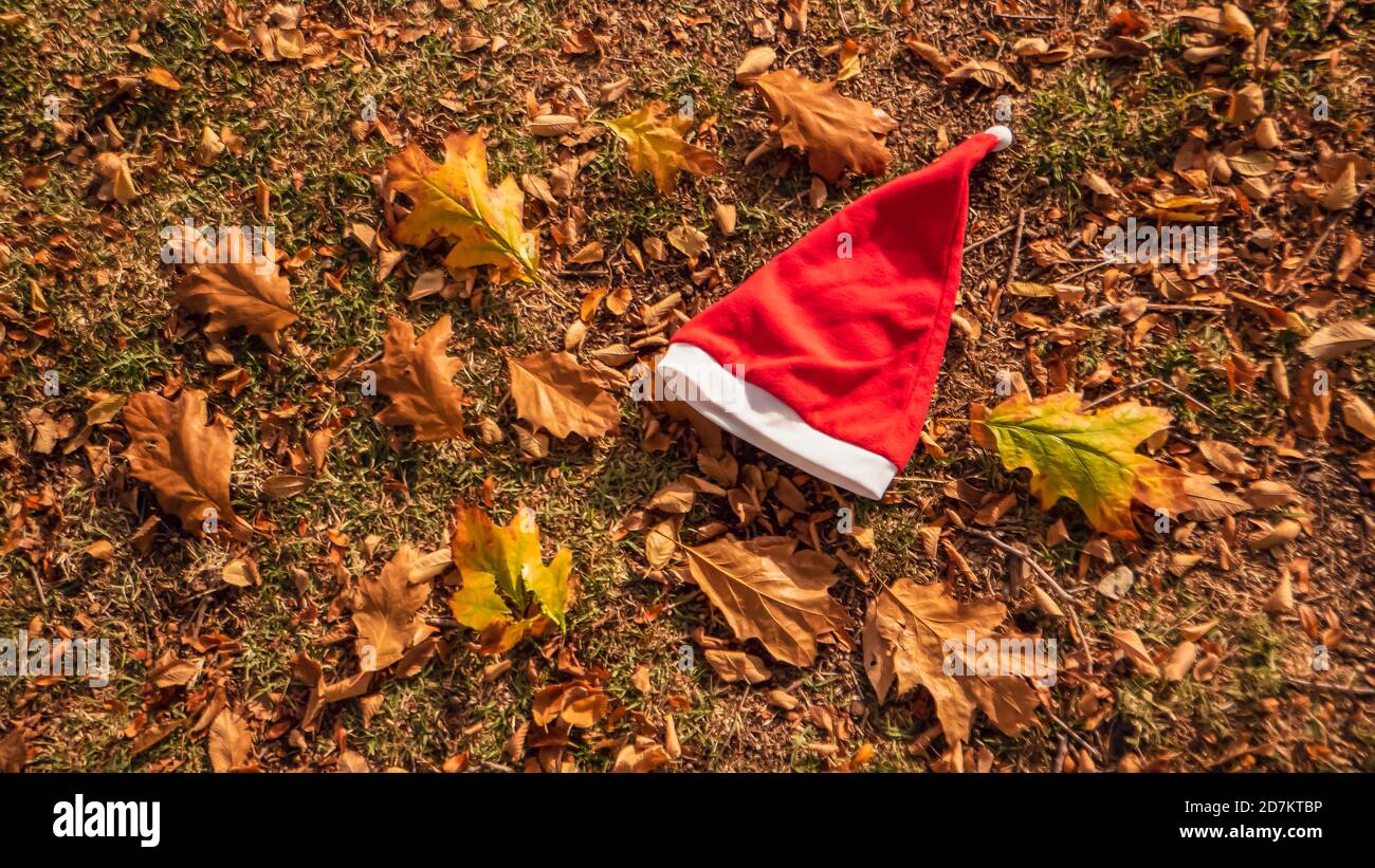 Weihnachten und Winter kommen bald. Ein konzeptuelles Hintergrundfoto des Weihnachtsmann-Hutes auf gelben Blättern im Herbst. Letzter Tag des Herbst- und Winterurlaubs Stockfoto