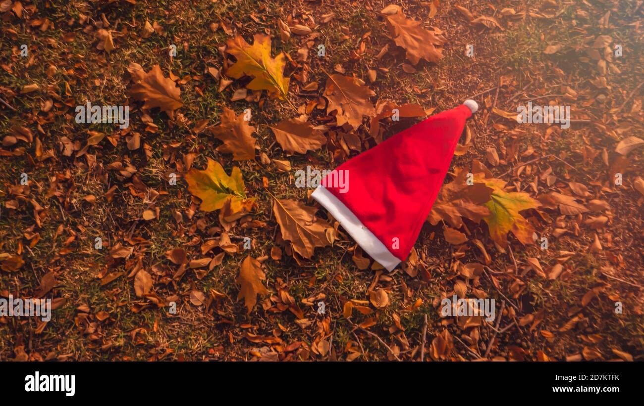 Weihnachten und Winter kommen bald. Ein konzeptuelles Hintergrundfoto des Weihnachtsmann-Hutes auf gelben Blättern im Herbst. Letzter Tag des Herbst- und Winterurlaubs Stockfoto