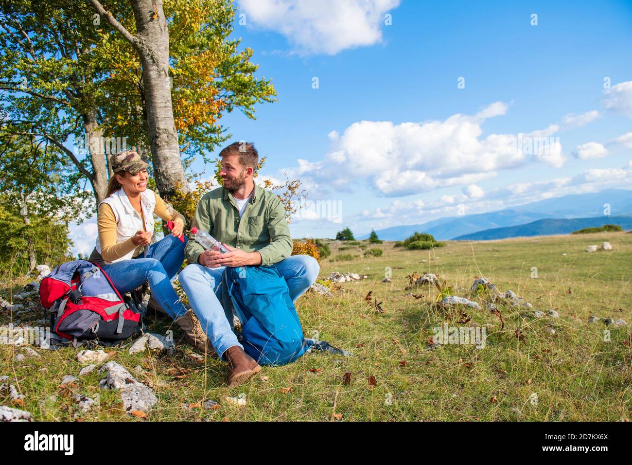 Junges Paar Trinkwasser, während er auf den Felsen während der Reisen in die Berge Stockfoto