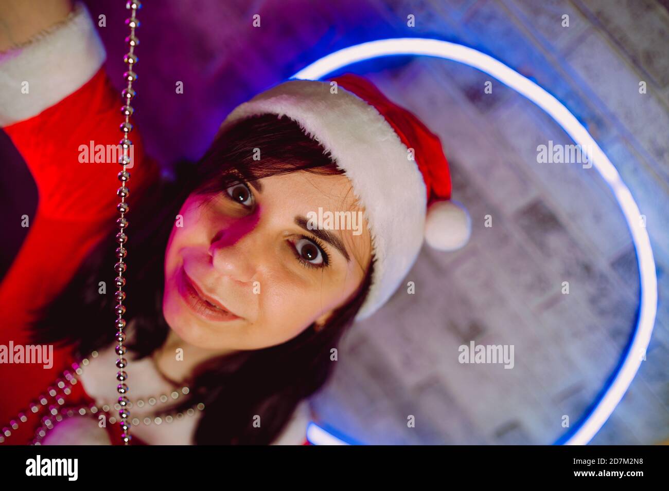 Porträt einer jungen Frau im Weihnachtsmann-Anzug mit Perlen an der beleuchteten Wand. Nahaufnahme von hübschen Weibchen in Weihnachtsmütze mit Perlen. Konzept von Stockfoto