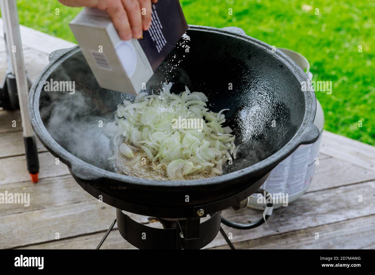 Mann gießt Paprika in Gulasch in einem Kessel im Freien. Stockfoto
