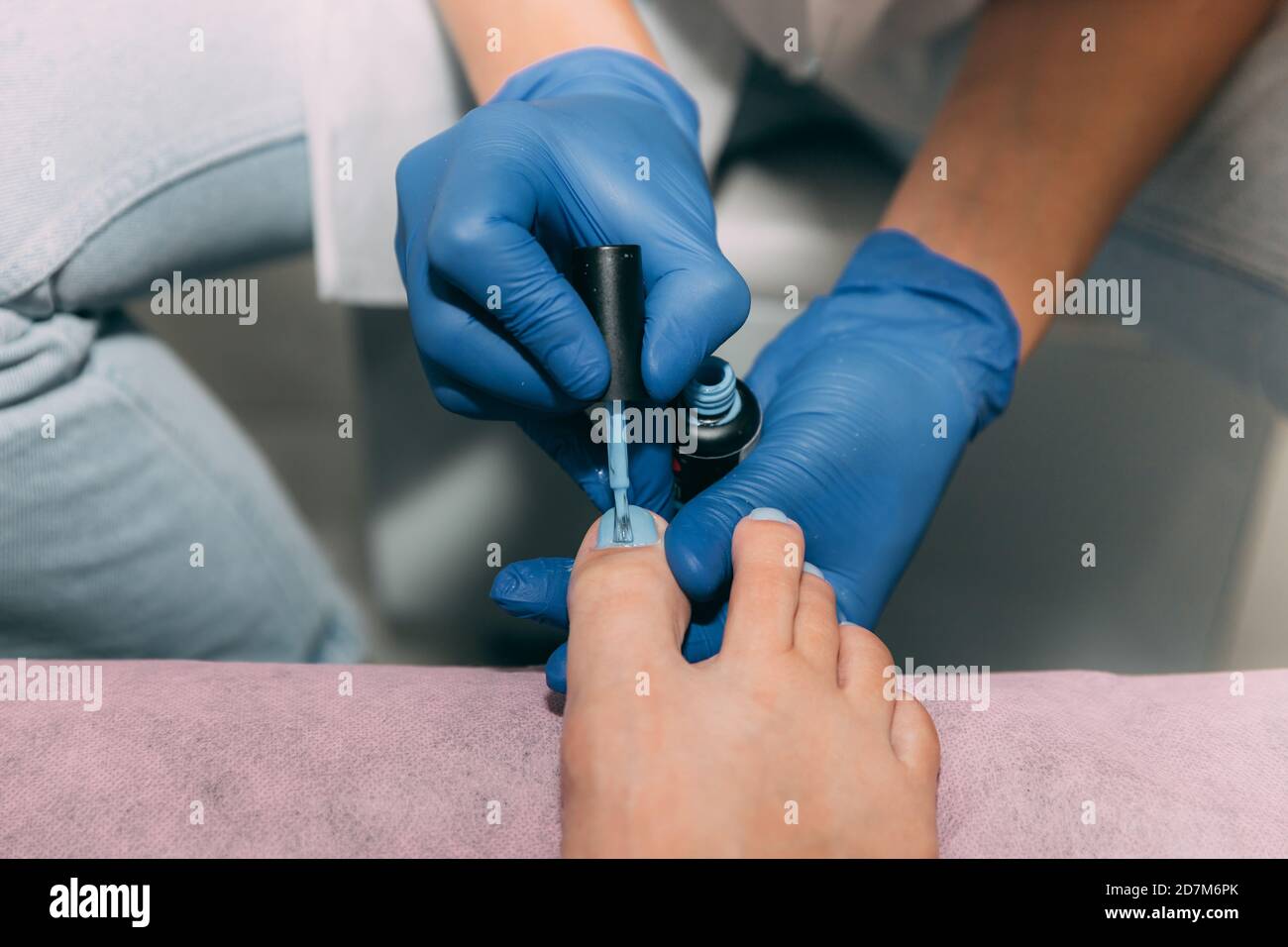 Pediküre Prozess im Salon. Fußpflege Behandlung und Nagel. Gelpolitur mit einem Pinsel auf die Nägel auftragen. Master in blauen Handschuhen macht Pediküre mit Maniküre Stockfoto