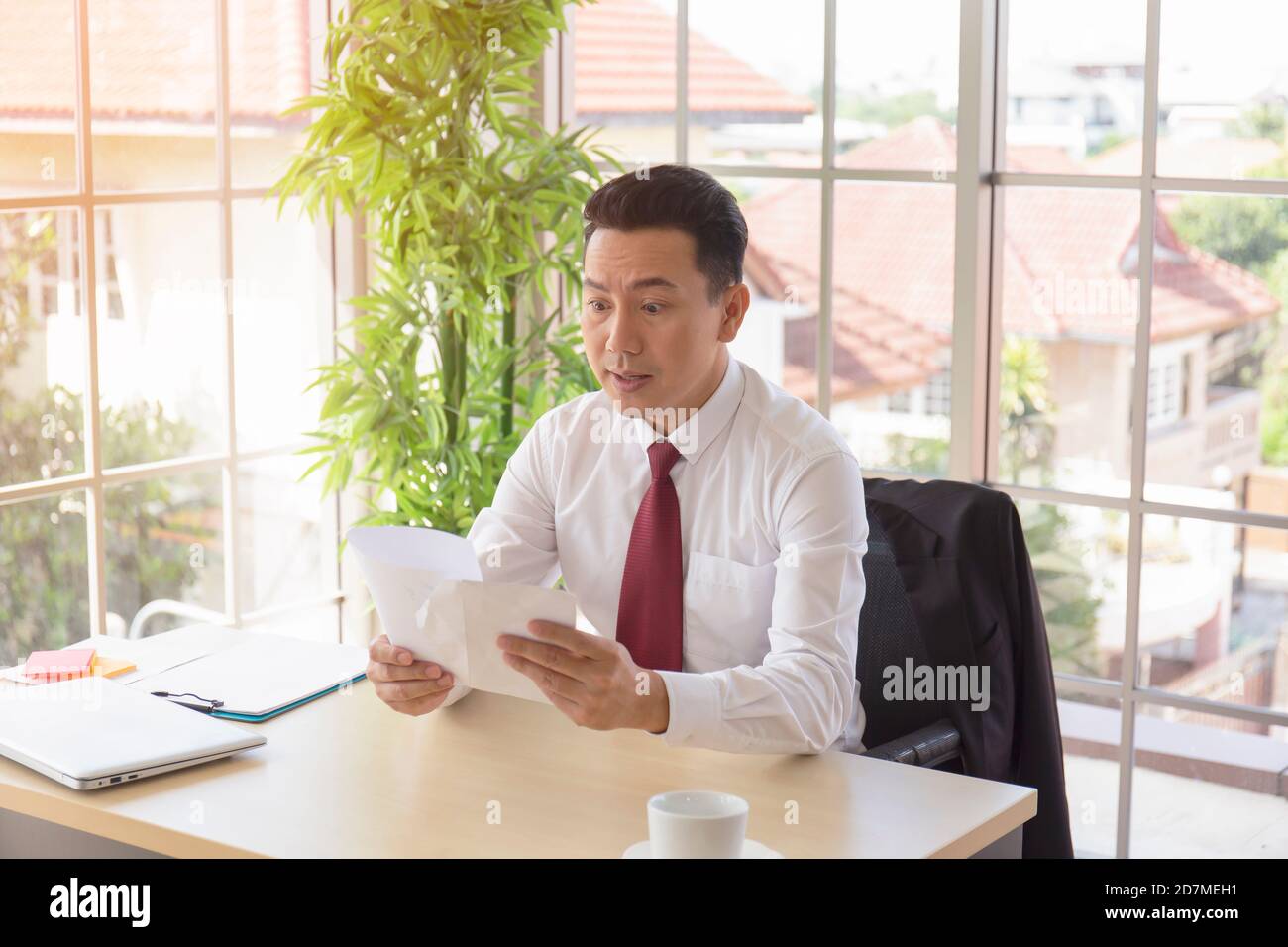 Ein Mann in einer asiatischen Firma erhält mit schockierter Äußerung wichtige Dokumente auf seinem Schreibtisch. Stockfoto