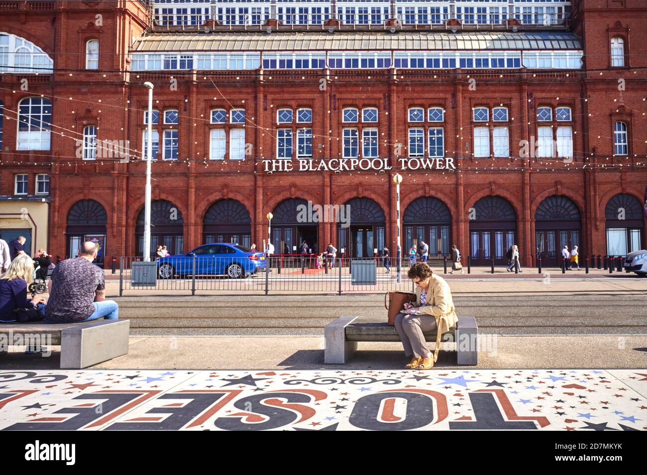 Eine ältere Frau saß und schrieb vor dem Blackpool Tower Gebäude Stockfoto