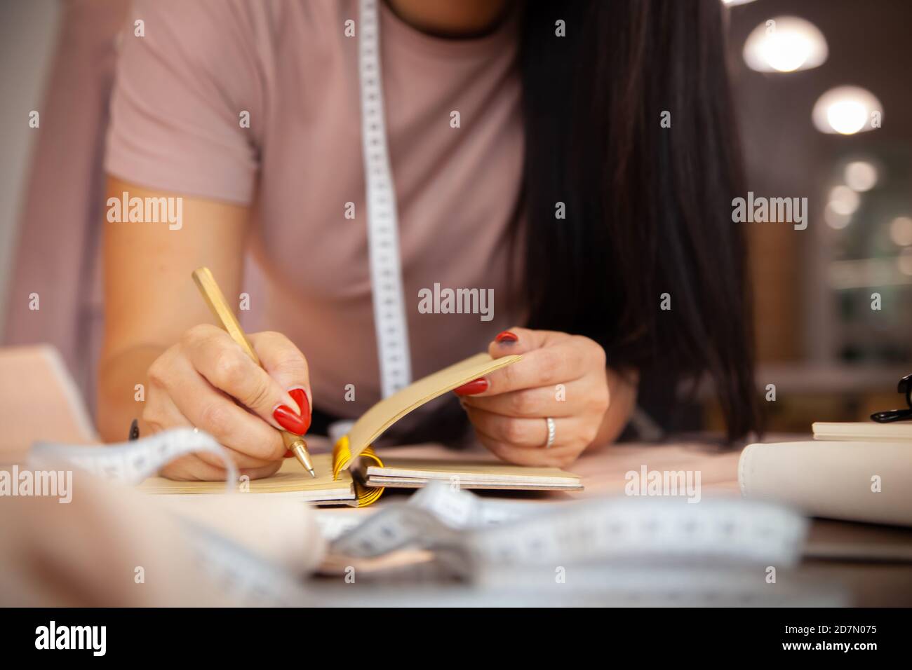 Schöne junge Frau Designer macht Notizen von Kleidung Messungen Auf Notizbuch im Nähstudio Stockfoto