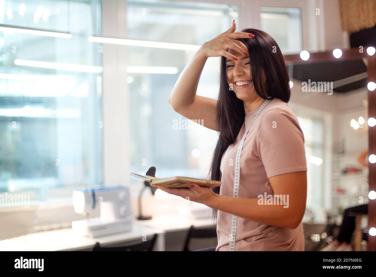 Schöne junge Frau lächelt und lernt Notizen zu machen Von Bekleidungsmessungen auf Nähklasse Stockfoto