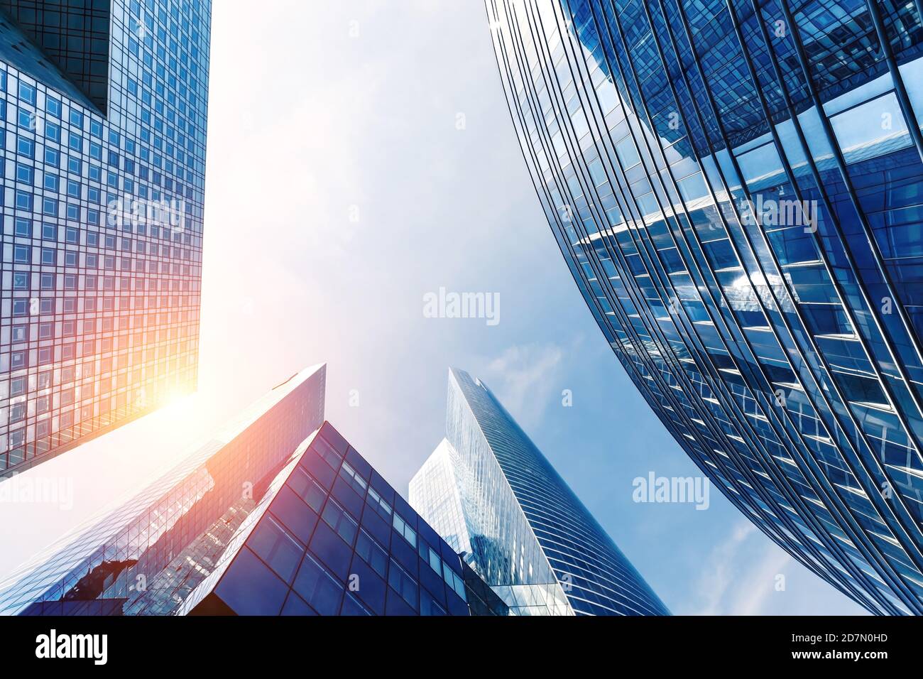 Bürogebäude im Finanzviertel mit Sonnenlicht und Himmel, die sich in den modernen Glaswänden von Wolkenkratzern spiegeln. Geschäftshintergrund. Niedriger V-Winkel Stockfoto