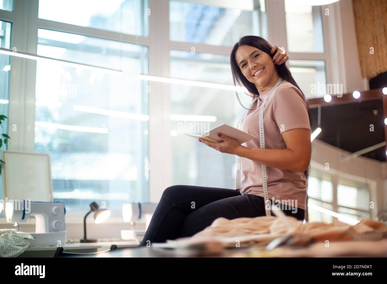 Schöne junge Frau lächelt und lernt Notizen zu machen Von Bekleidungsmessungen auf Nähklasse Stockfoto