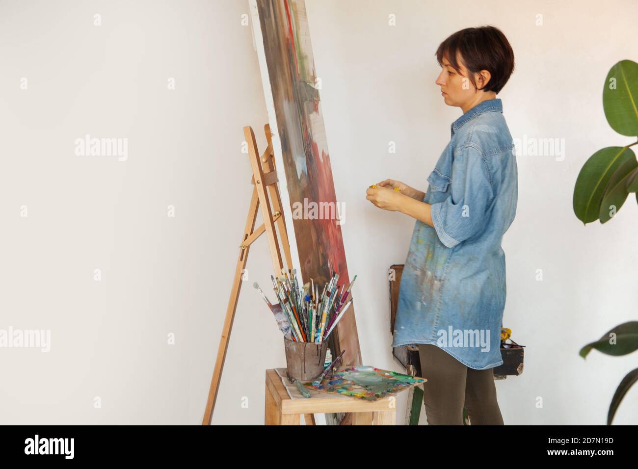 Junge Künstlerin hält Pinsel und Malerei mit Ölfarbe Auf gerahmter Baumwollleinwand auf Staffelei Stockfoto