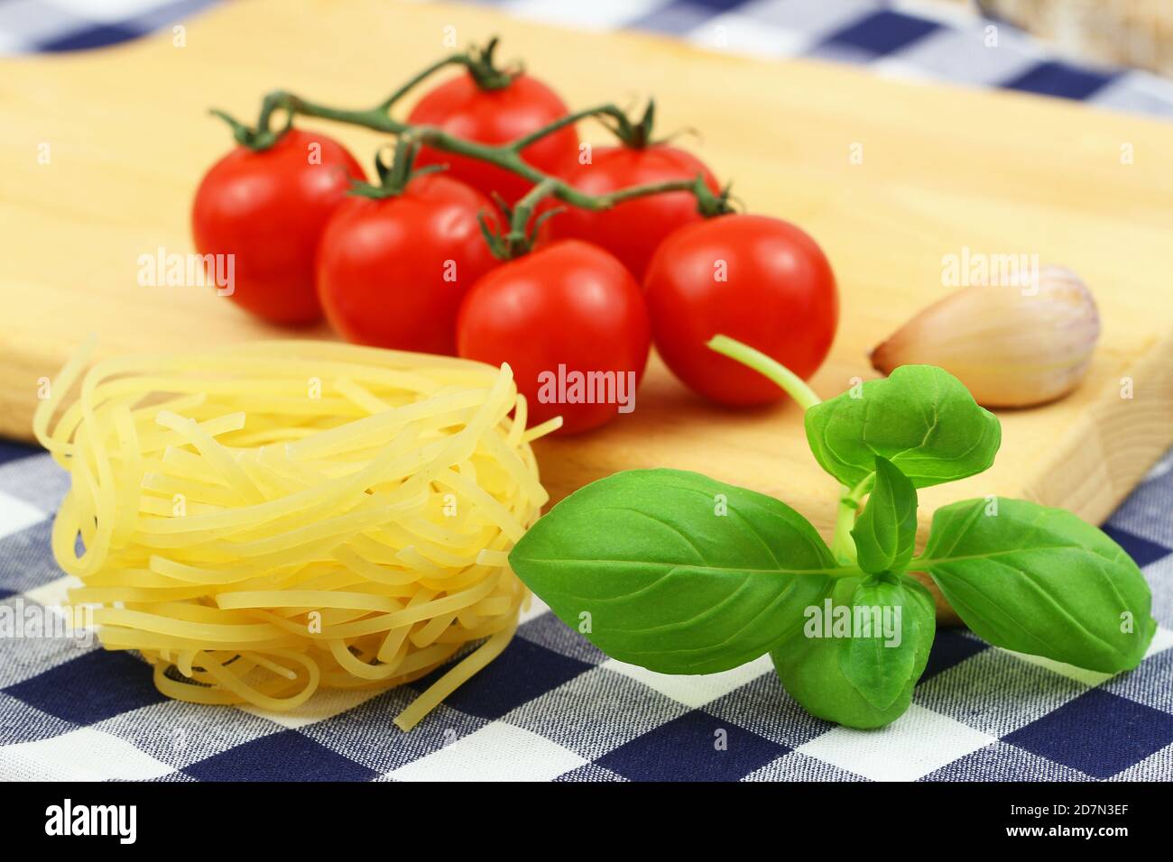 Pasta-Zutaten: Ungekochte Tagliatelle, Kirschtomaten auf Stiel und frische Basilikumblätter Stockfoto