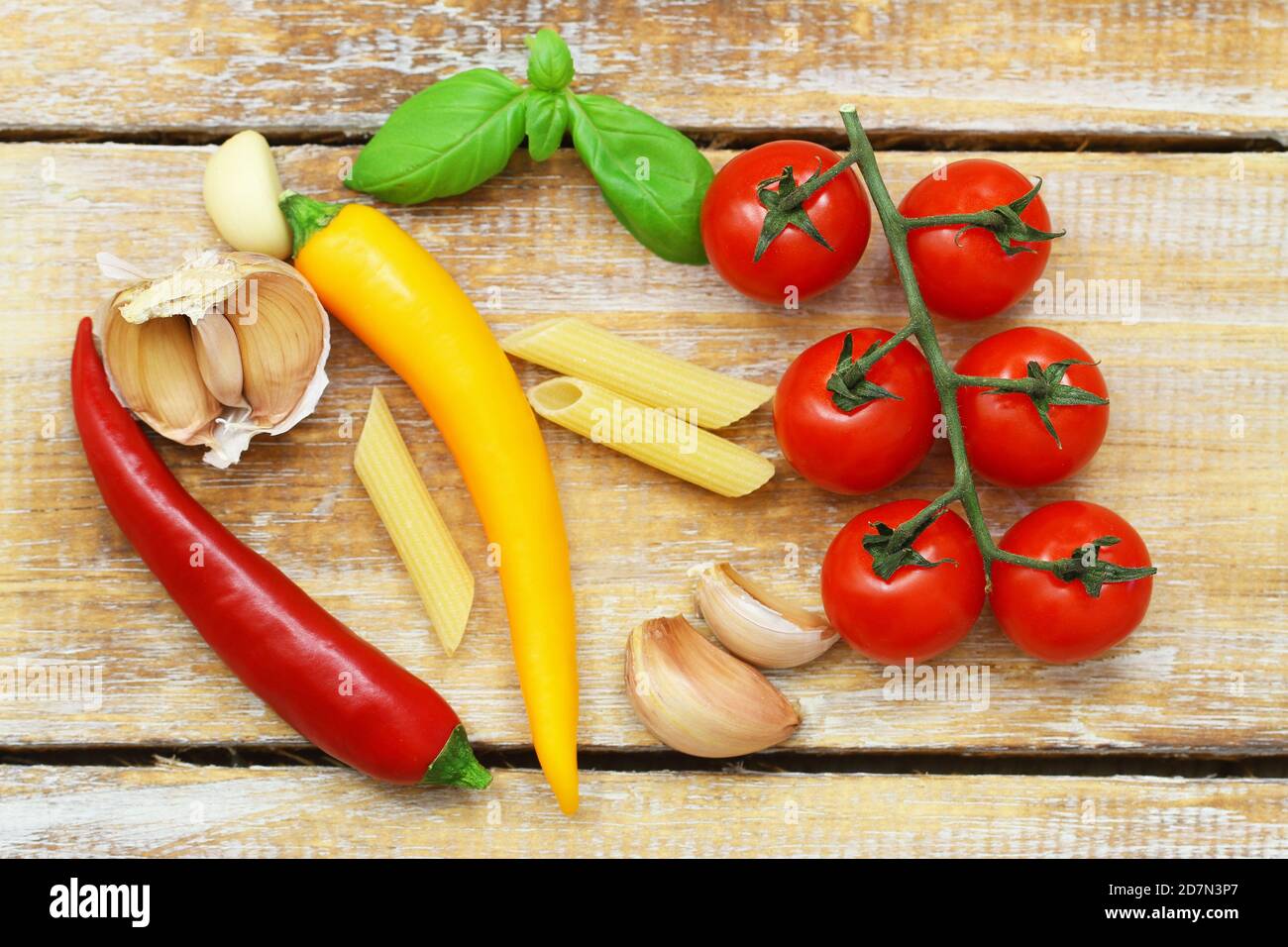 Auswahl an Zutaten: Ungekochte Pasta, Kirschtomaten, Knoblauchzehen, frische Basilikumblätter, Chilies auf Holzoberfläche Stockfoto