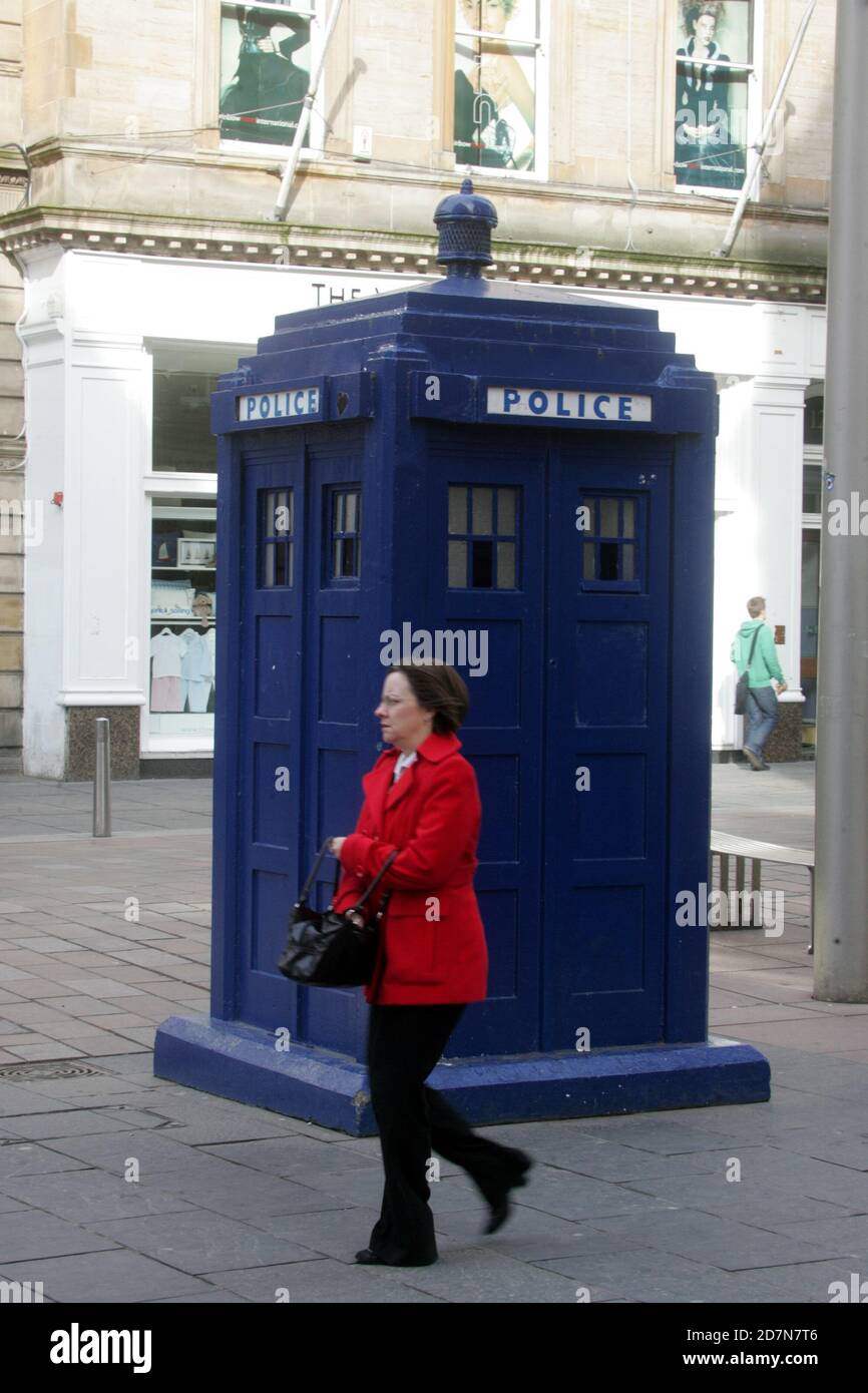 Frau in rotem Mantel kommt an der Polizeibox ( Tardis Style ) in der Buchanan St, Glasgow vorbei Stockfoto