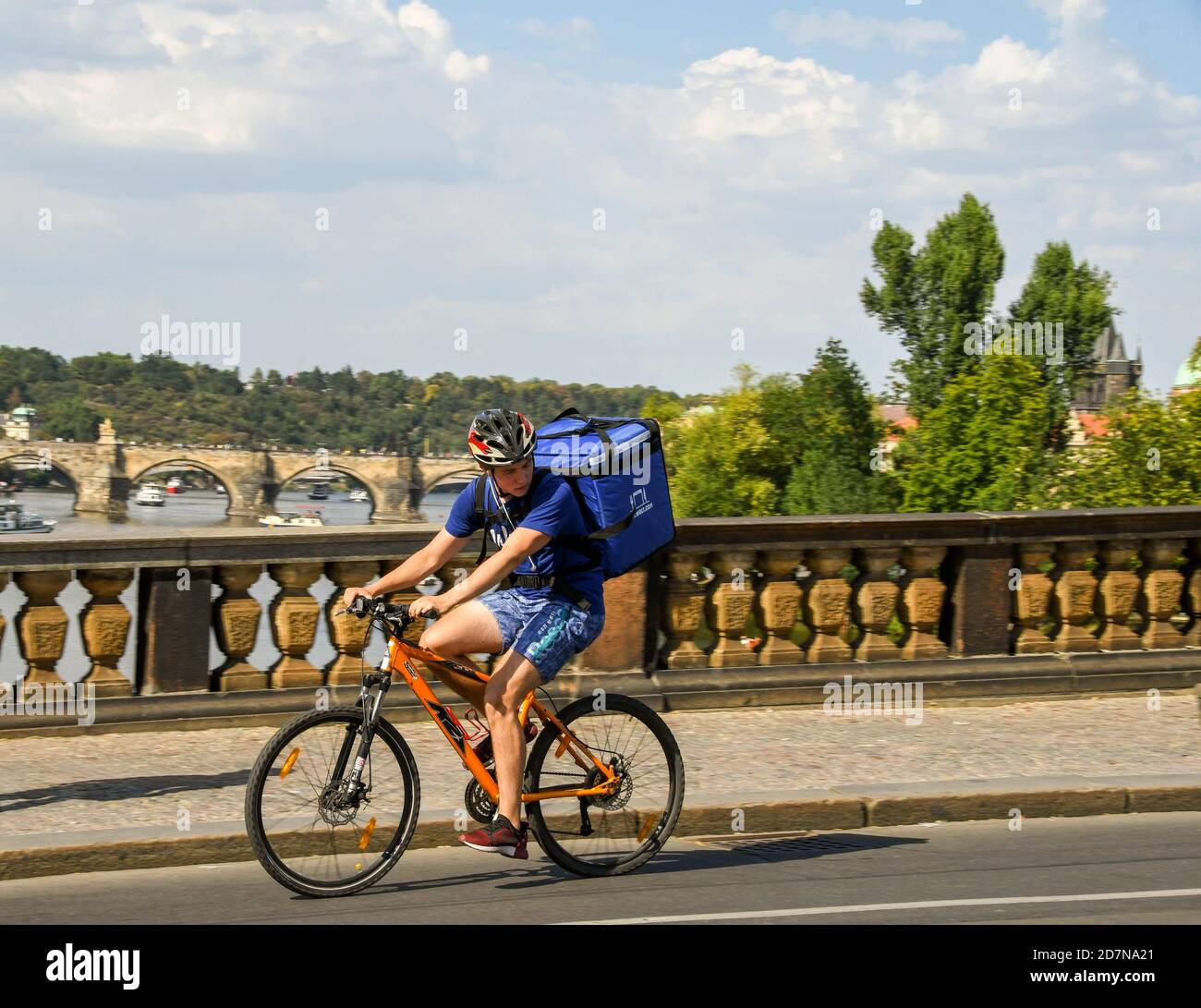 PRAG, TSCHECHISCHE REPUBLIK - AUGUST 2018: Person, die mit dem Fahrrad über eine Brücke im Prager Stadtzentrum fährt, mit einem Lieferpaket auf dem Rücken. Stockfoto