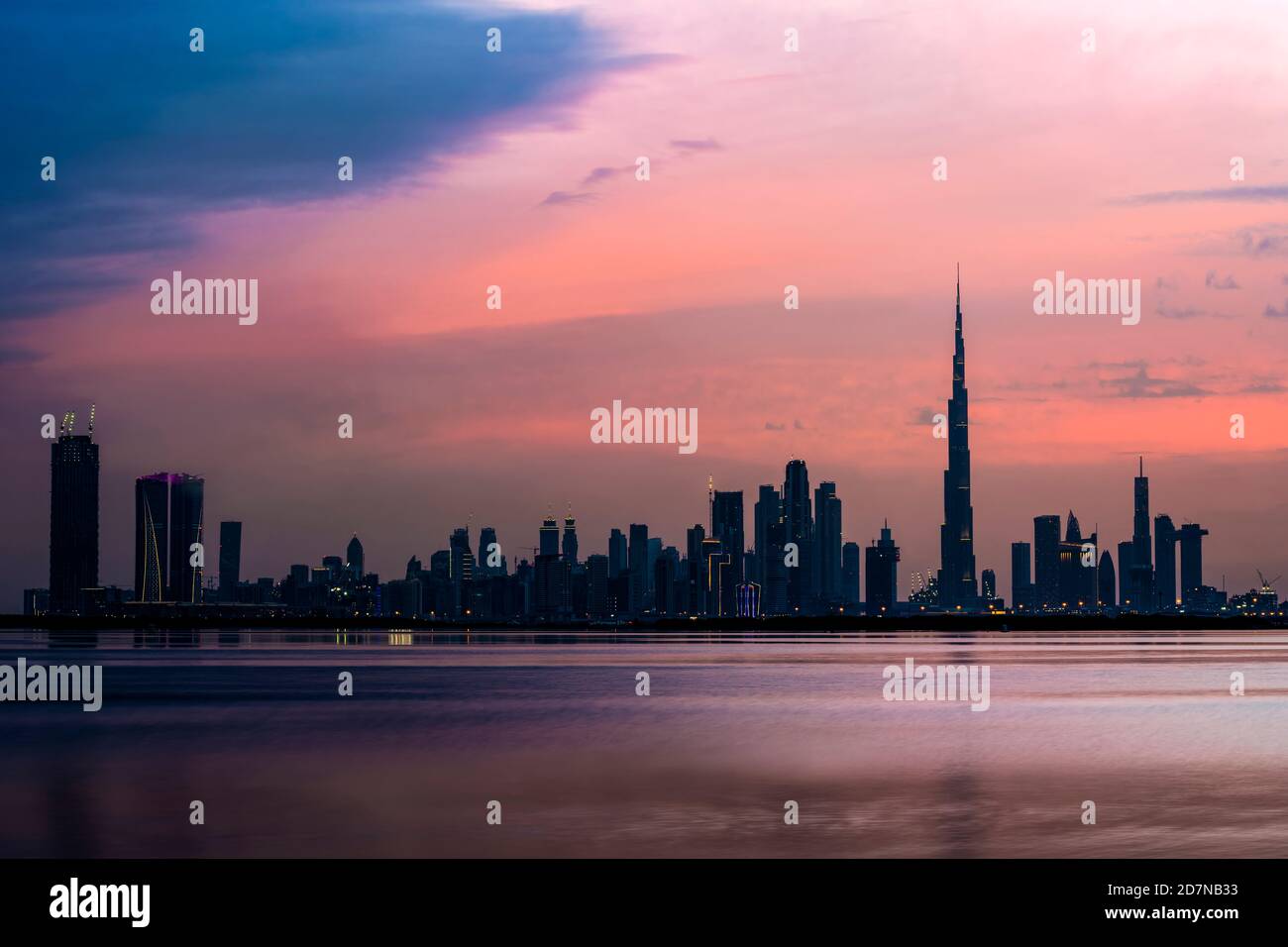 Atemberaubender Blick auf die beleuchtete Skyline von Dubai in der Abenddämmerung mit dem herrlichen Burj Khalifa und dem im Vordergrund fließenden Wasserkanal. Stockfoto